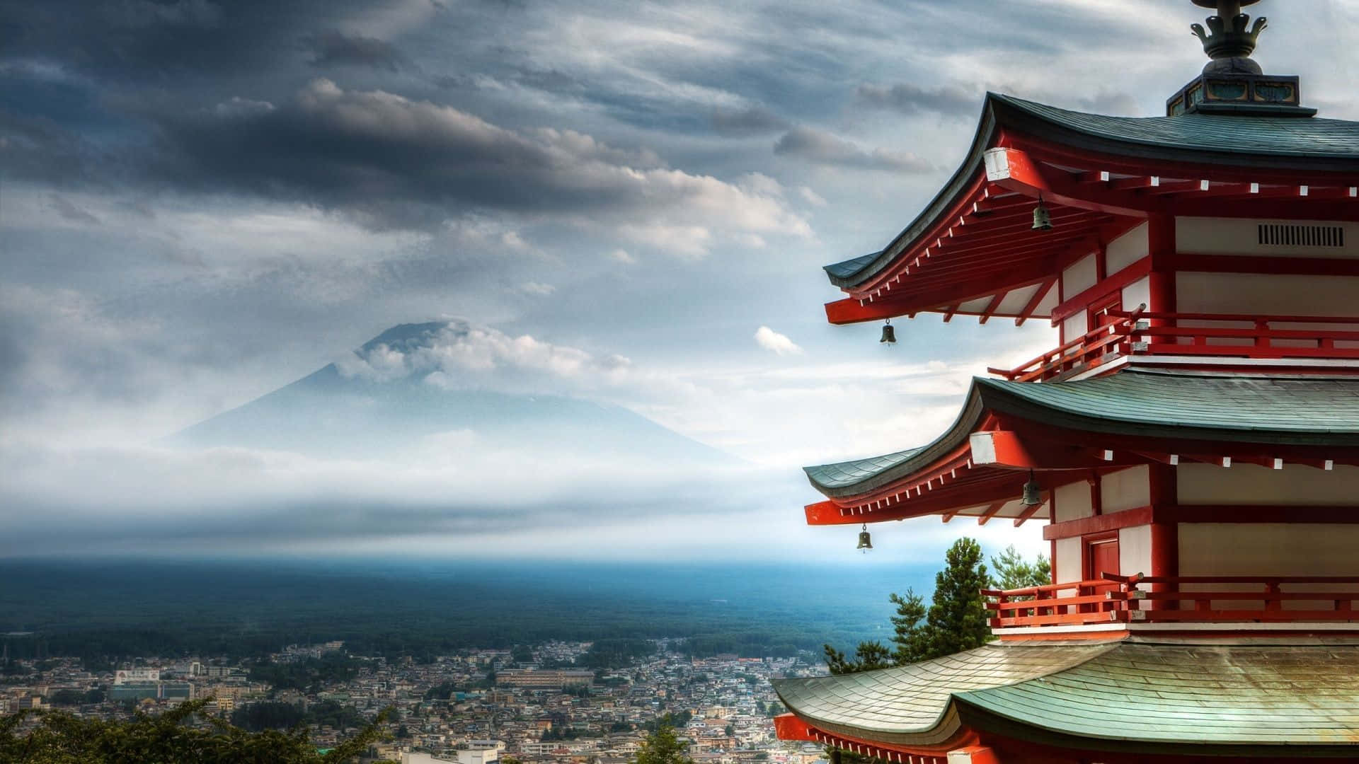 Shinto 桌布 壁紙 — 一座紅色日本塔俯瞰著霧濛濛的城市景觀，富士山在遠方雲層中雄偉地聳立。