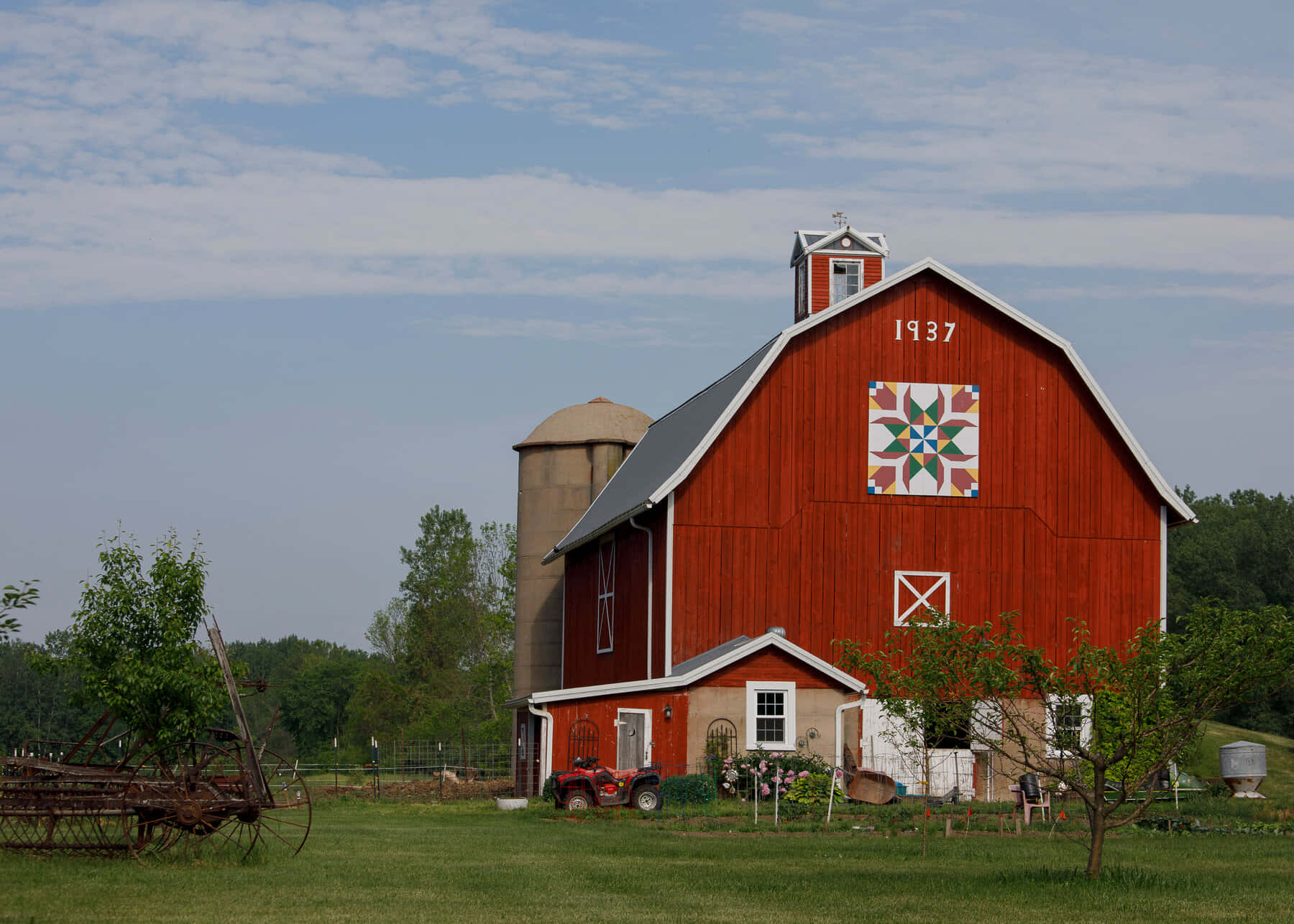 Barn 桌布 壁紙 — 一座經典的紅色穀倉，帶有拼布圖案和1937年的日期，矗立在部分多雲的天空下的綠色田野中。