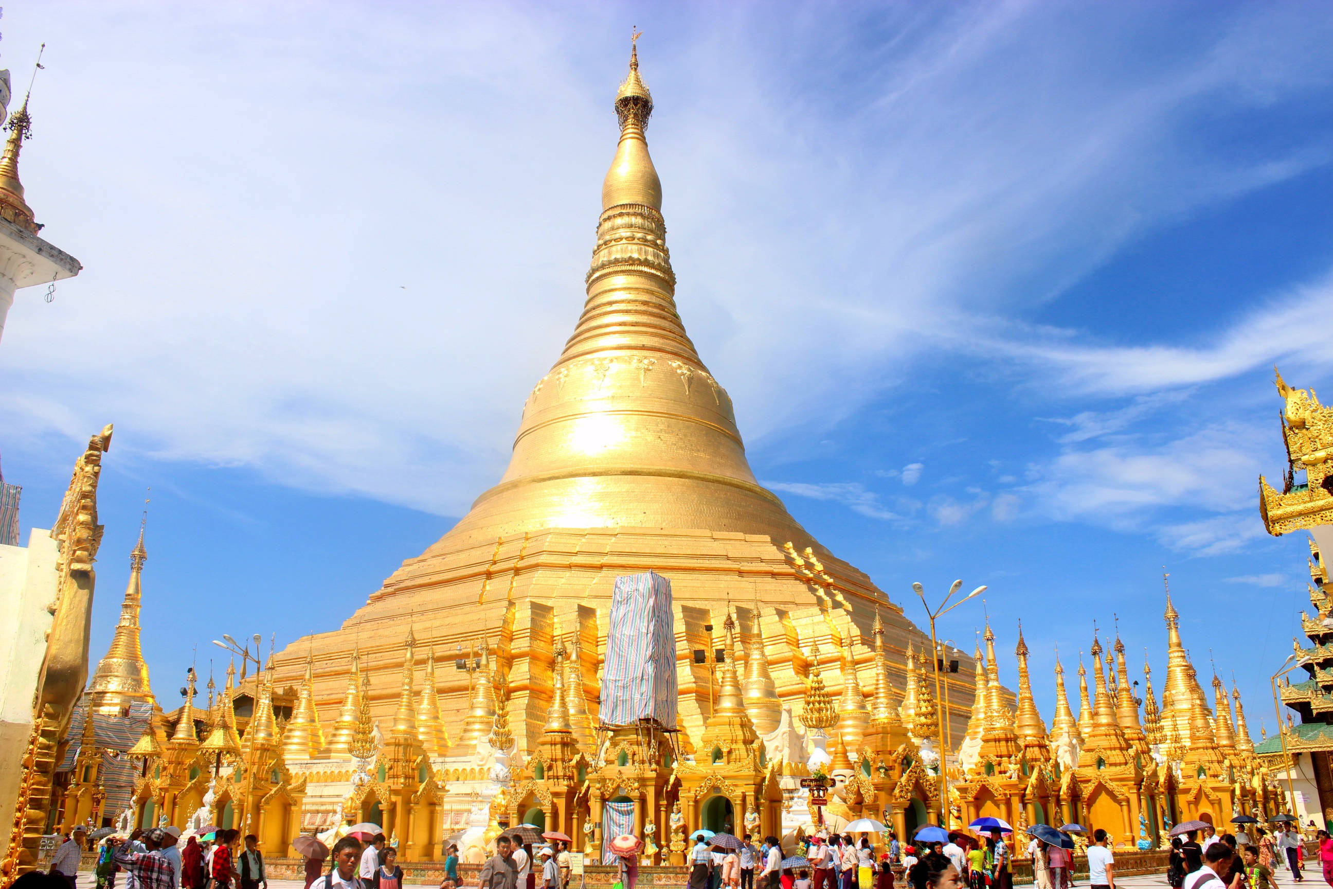 Yangon 桌布 壁紙 — 一座耀眼的金色寶塔，帶有精緻的尖頂，在晴朗的藍天和縷縷白雲下雄偉地聳立。