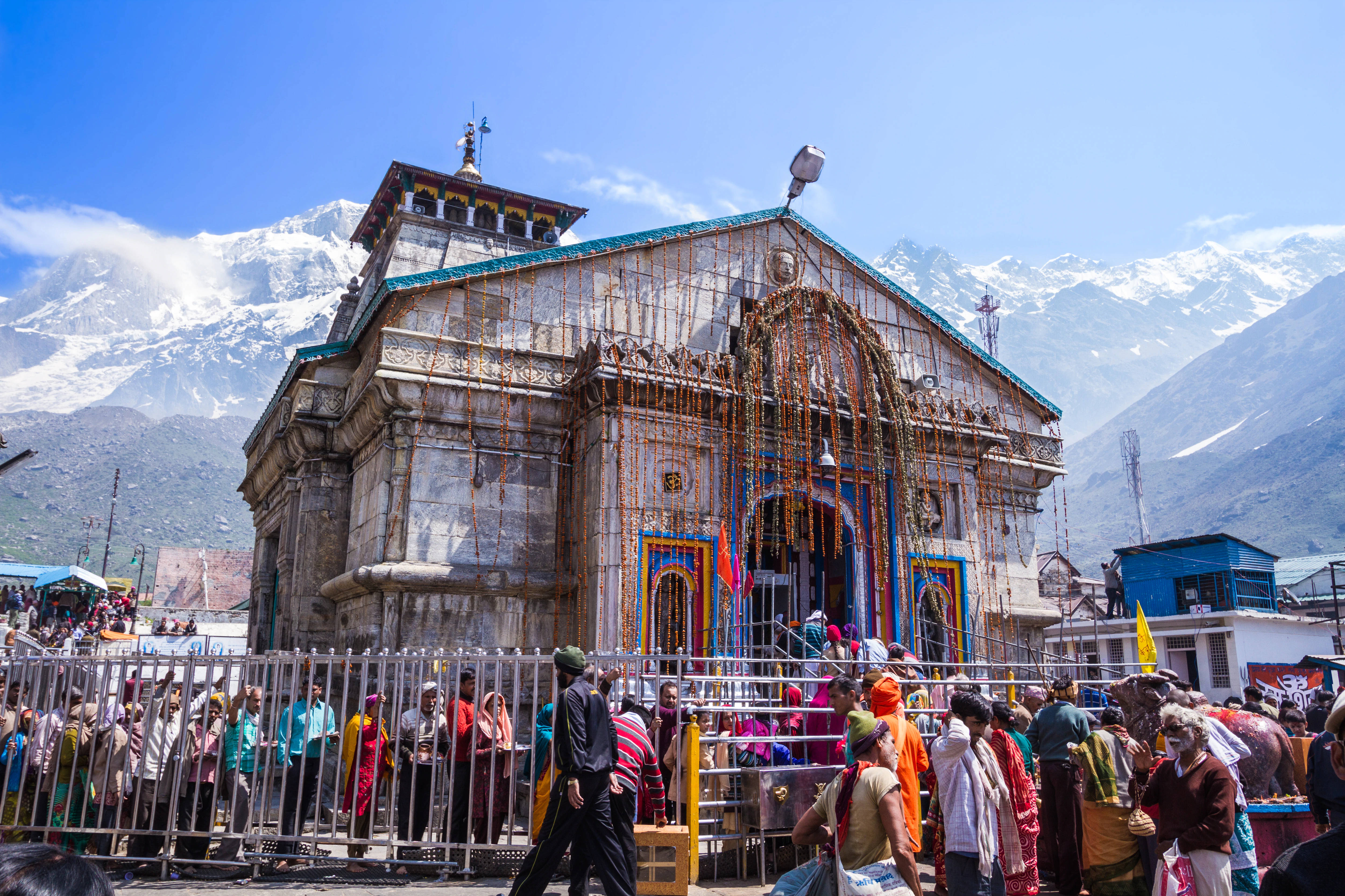 Kedarnath 桌布 壁紙 — 一座色彩繽紛、掛滿花環的寺廟矗立在雪山前，信徒們聚集在寺廟前。