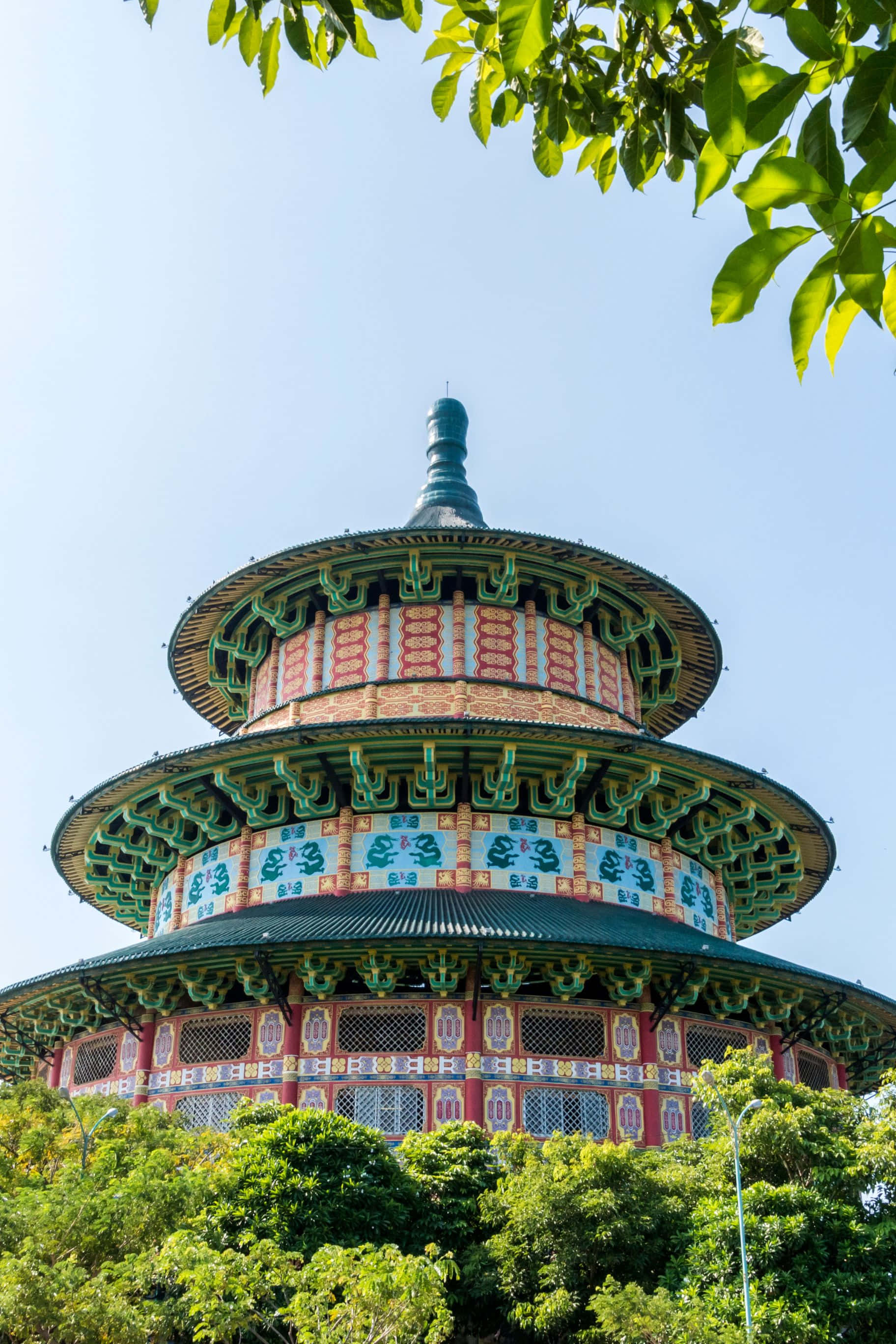 1824x2736 桌布 壁紙 — 一座色彩繽紛的多層傳統寶塔在晴朗的藍天下從茂密的綠葉中升起。