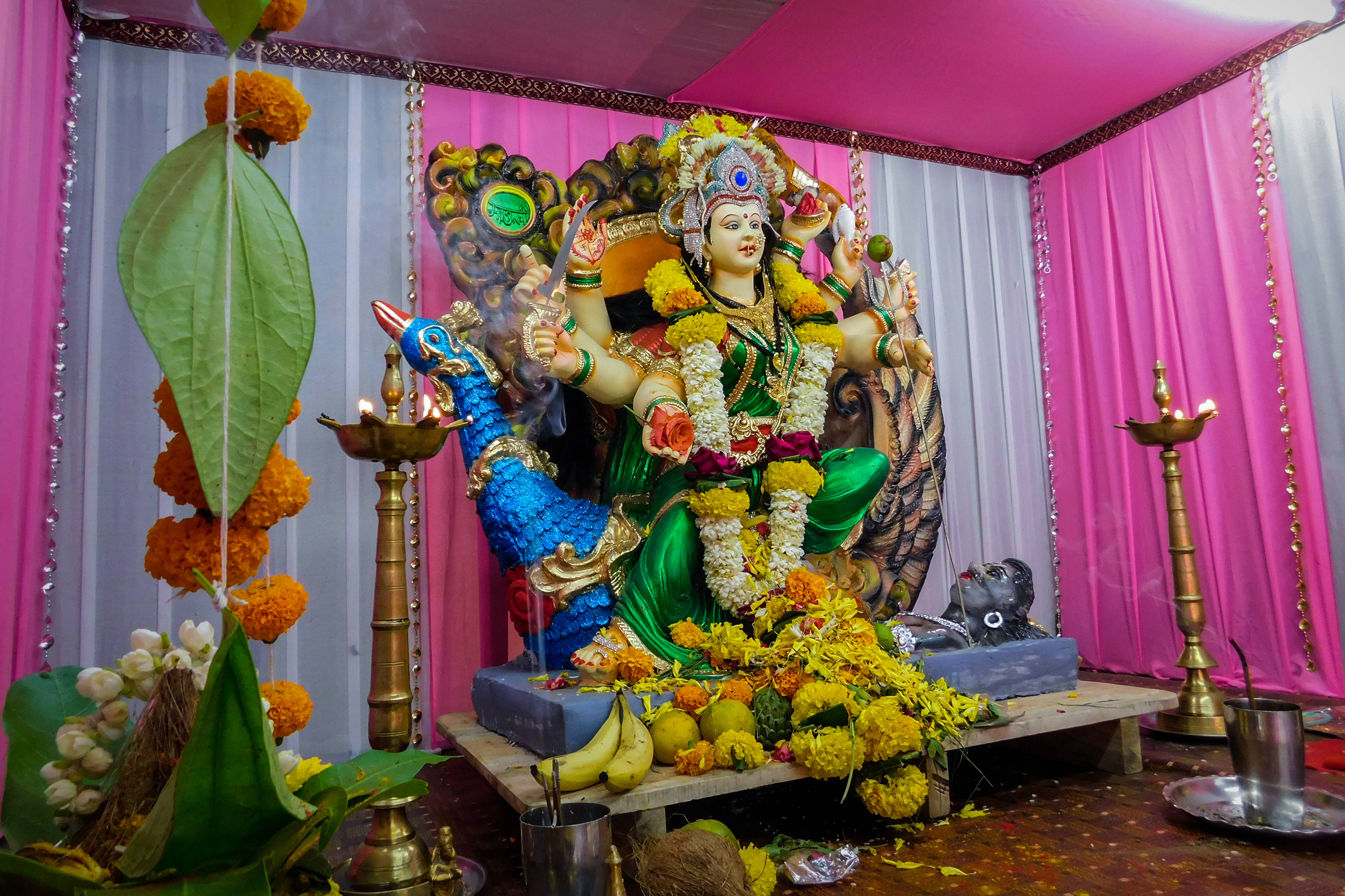 Navratri 桌布 壁紙 — 一座色彩鮮豔、多臂的印度教女神雕像，飾有萬壽菊和珠寶，坐在裝飾有粉紅色窗簾和點燃油燈的祭壇上。