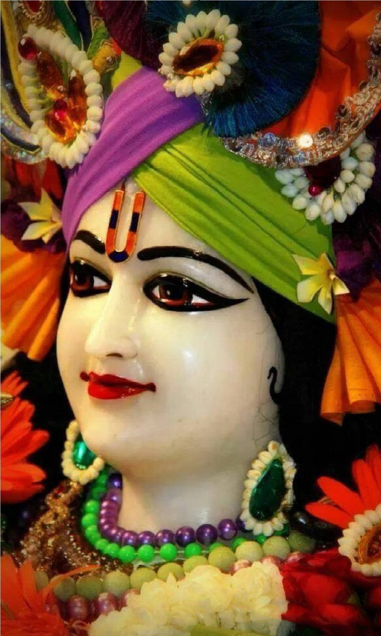 krishna phone 桌布 壁紙 — 一座色彩鮮豔、裝飾著彩色頭巾、珠寶和花朵的女神雕像，色調豐富。