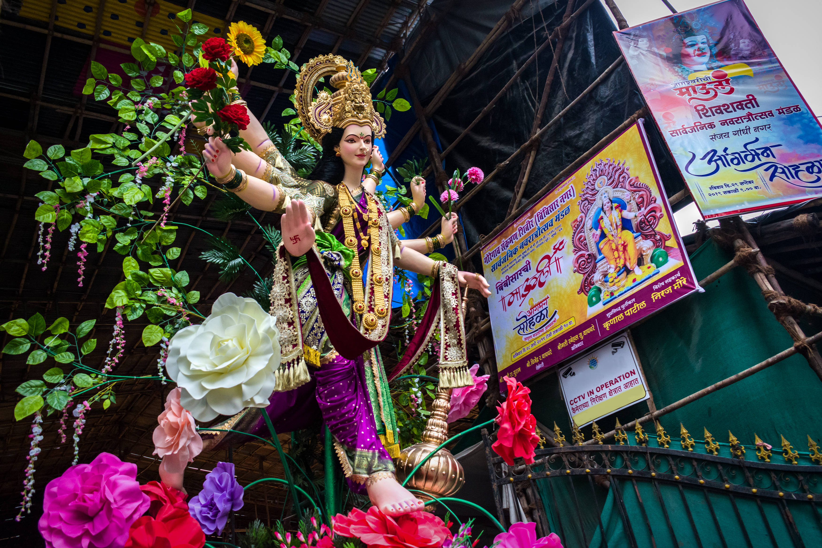 Navratri 桌布 壁紙 — 一座色彩鮮豔的多臂印度教女神雕像，飾有黃金珠寶，在華蓋下被五顏六色的鮮花環繞。