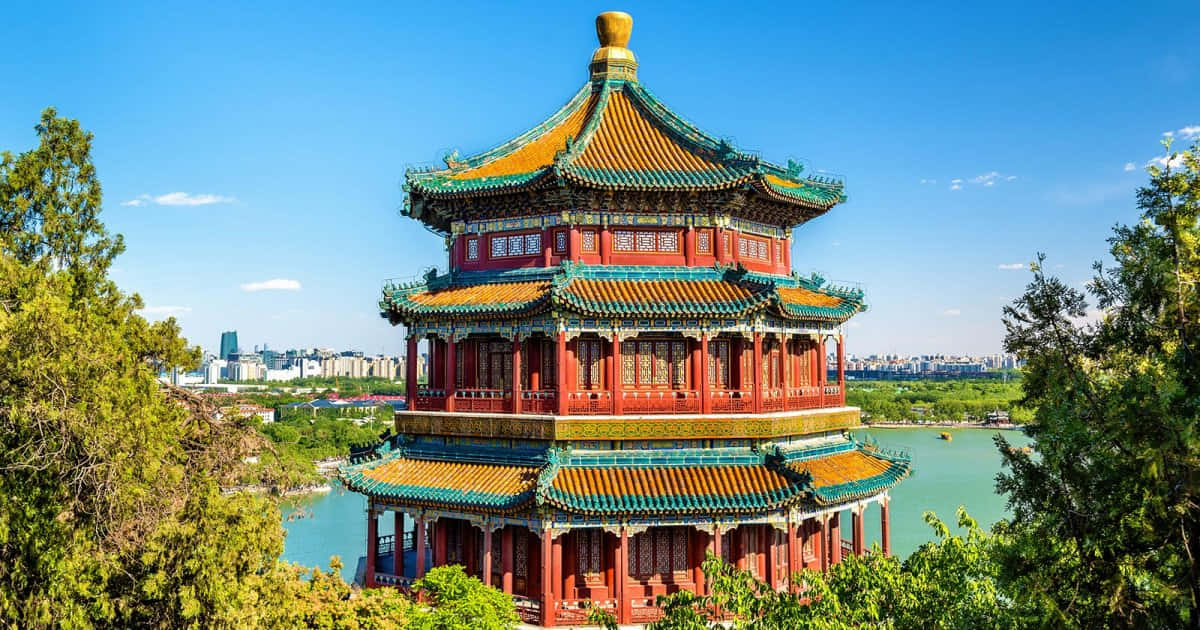 Tree 桌布 壁紙 — 一座色彩鮮豔的紅金色傳統中國寶塔，雄偉地矗立在寧靜的湖邊，周圍是茂密的綠樹，天空清澈湛藍。