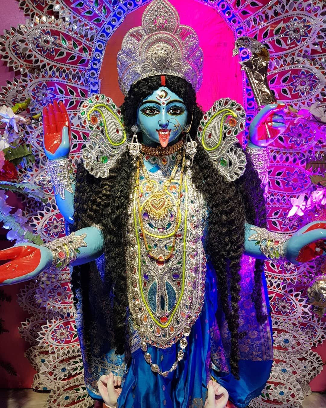 Goddess 桌布 壁紙 — 一座色彩鮮豔的藍色女神雕像，有多隻手臂和華麗的珠寶，站在發光的粉紅色和紫色圖案背景前。