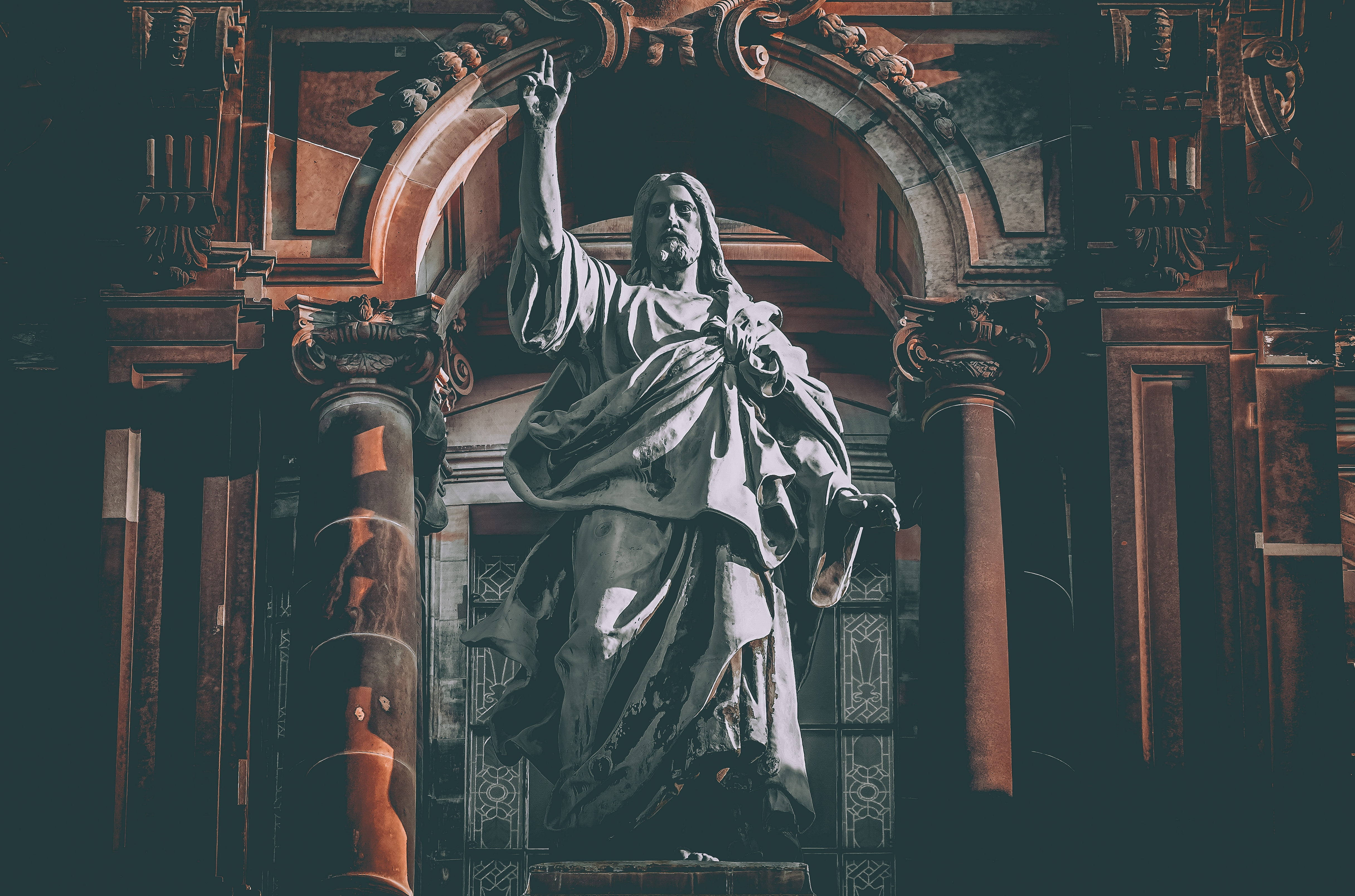 Christ 桌布 壁紙 — 一座莊嚴的耶穌基督石像，舉起手，站在光線昏暗的大教堂內一個裝飾華麗的拱形壁龕下。