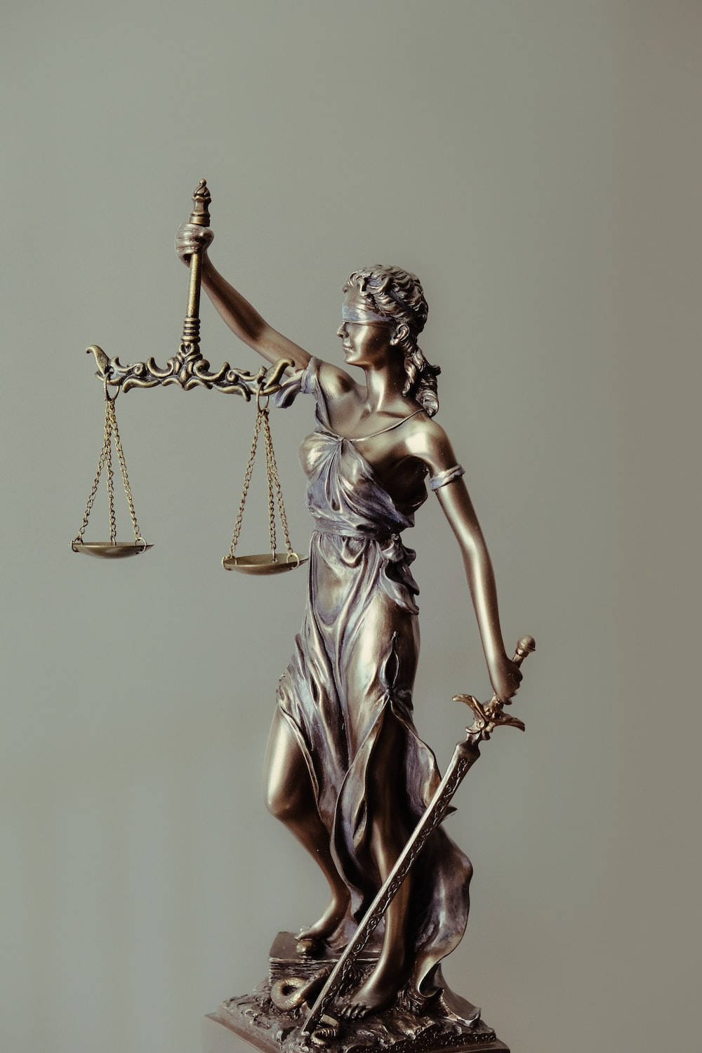 Advocate 桌布 壁紙 — 一座蒙著雙眼的正義女神青銅雕像，手持天秤和劍，背景為純灰色。