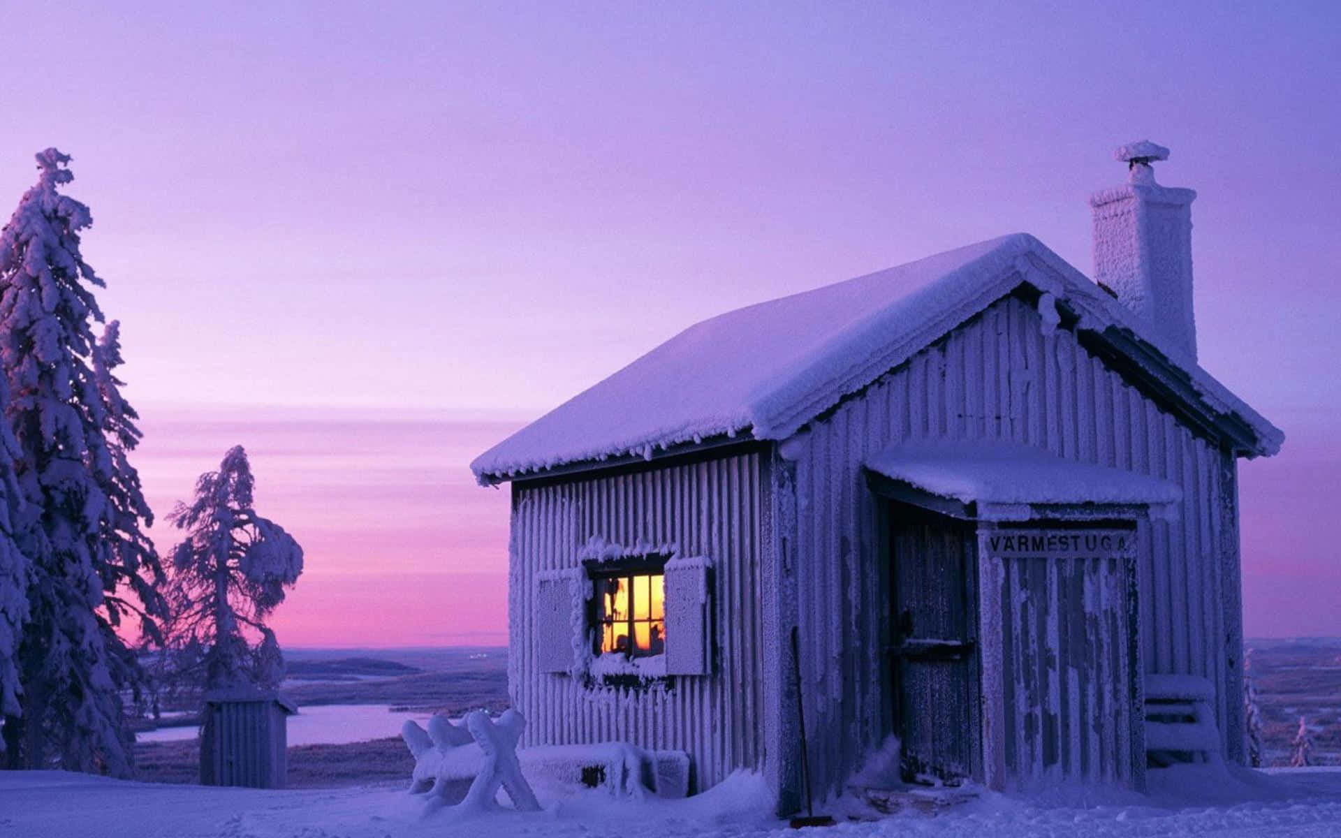 Evening 桌布 壁紙 — 一座被雪覆蓋的木屋，窗戶透出光芒，獨自矗立在冰凍的風景中，背景是紫粉色的暮色天空。