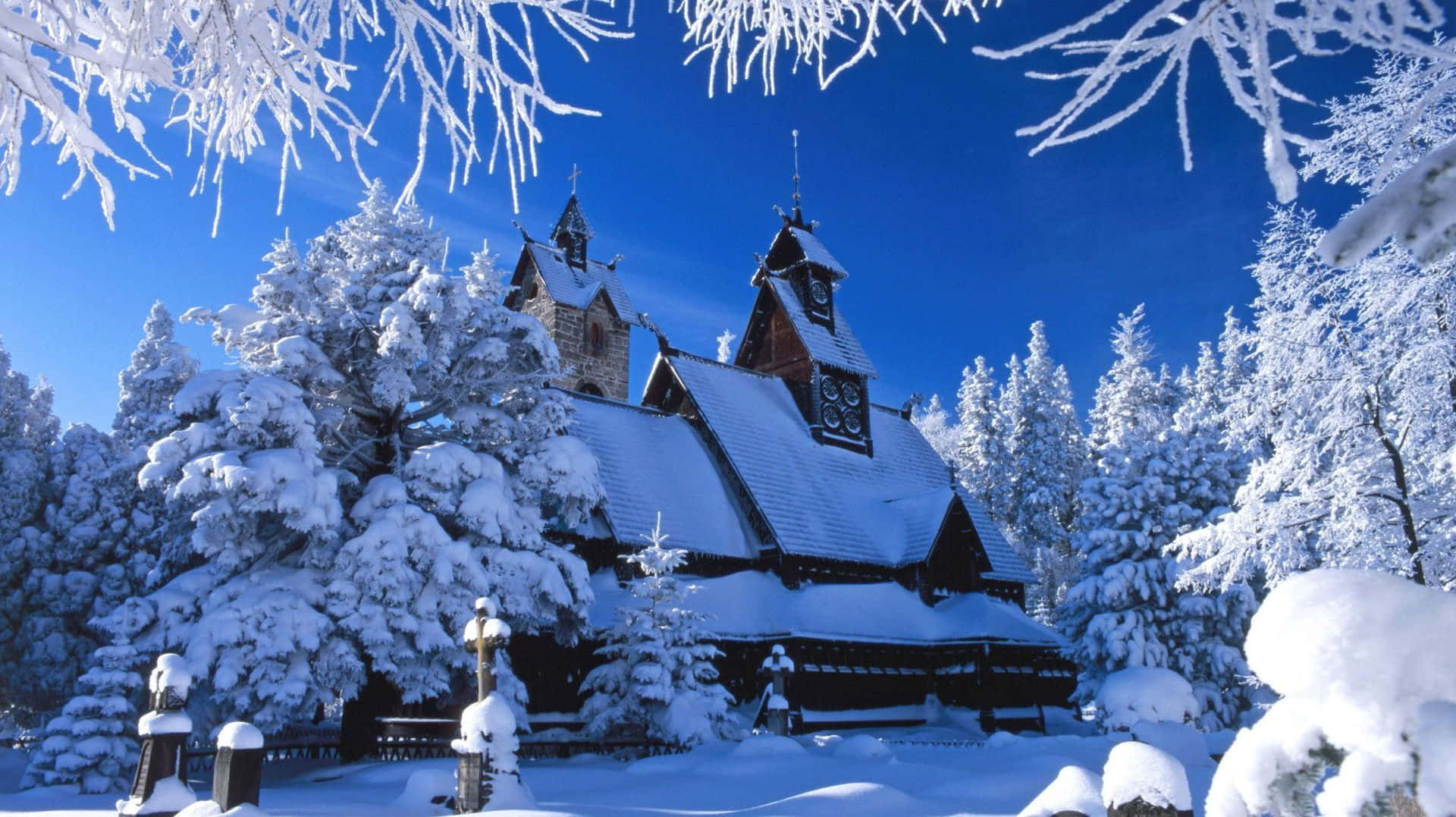 冬季美學 桌布 壁紙 — 一座被雪覆蓋的木造教堂，擁有精緻的建築風格，在晴朗的藍天下，被結霜的樹枝環繞，顯得寧靜祥和。
