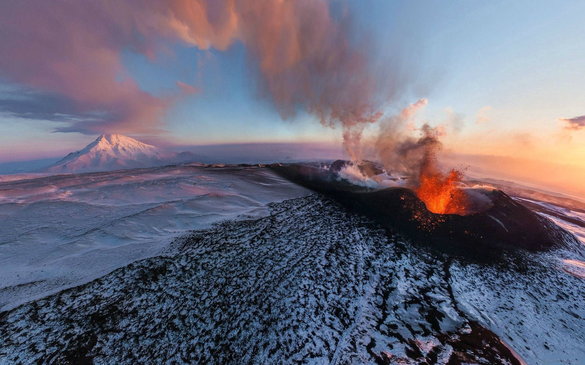 日落 桌布 壁紙 — 一座被雪覆蓋的火山噴發出熾熱的熔岩，背景是粉紅色和藍色雲彩繪成的暮色天空。