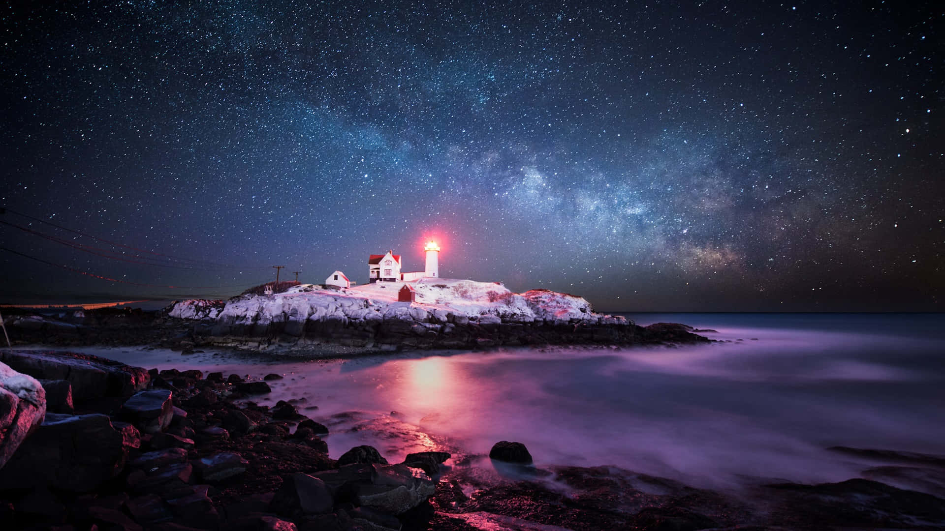 Lighthouse 桌布 壁紙 — 一座被雪覆蓋的燈塔在繁星點點的夜空下發出紅光，銀河在平靜的水面上拱起。