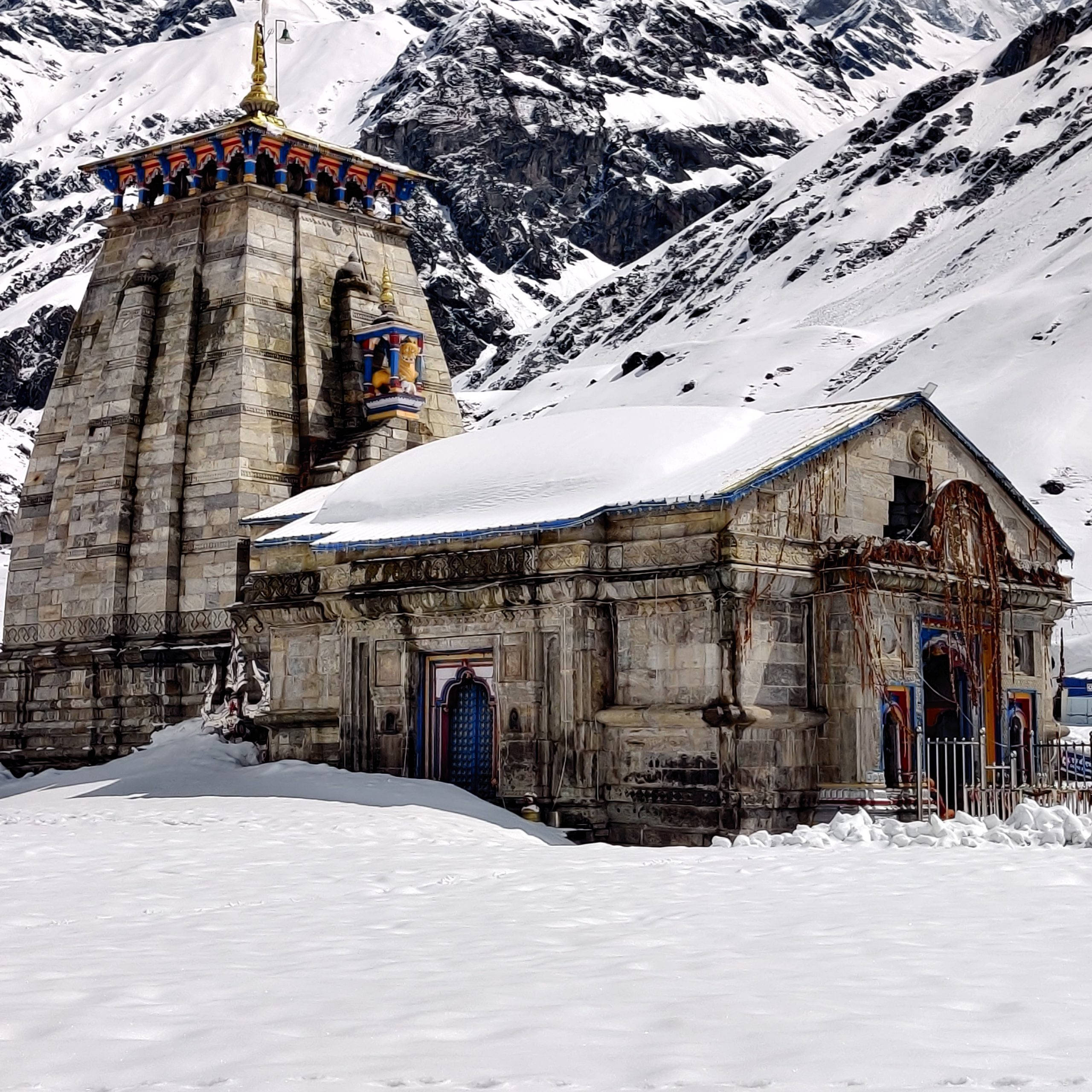 Kedarnath 桌布 壁紙 — 一座被雪覆蓋的石廟，帶有色彩繽紛的點綴，莊嚴地矗立在崎嶇、積雪的山脈背景下。