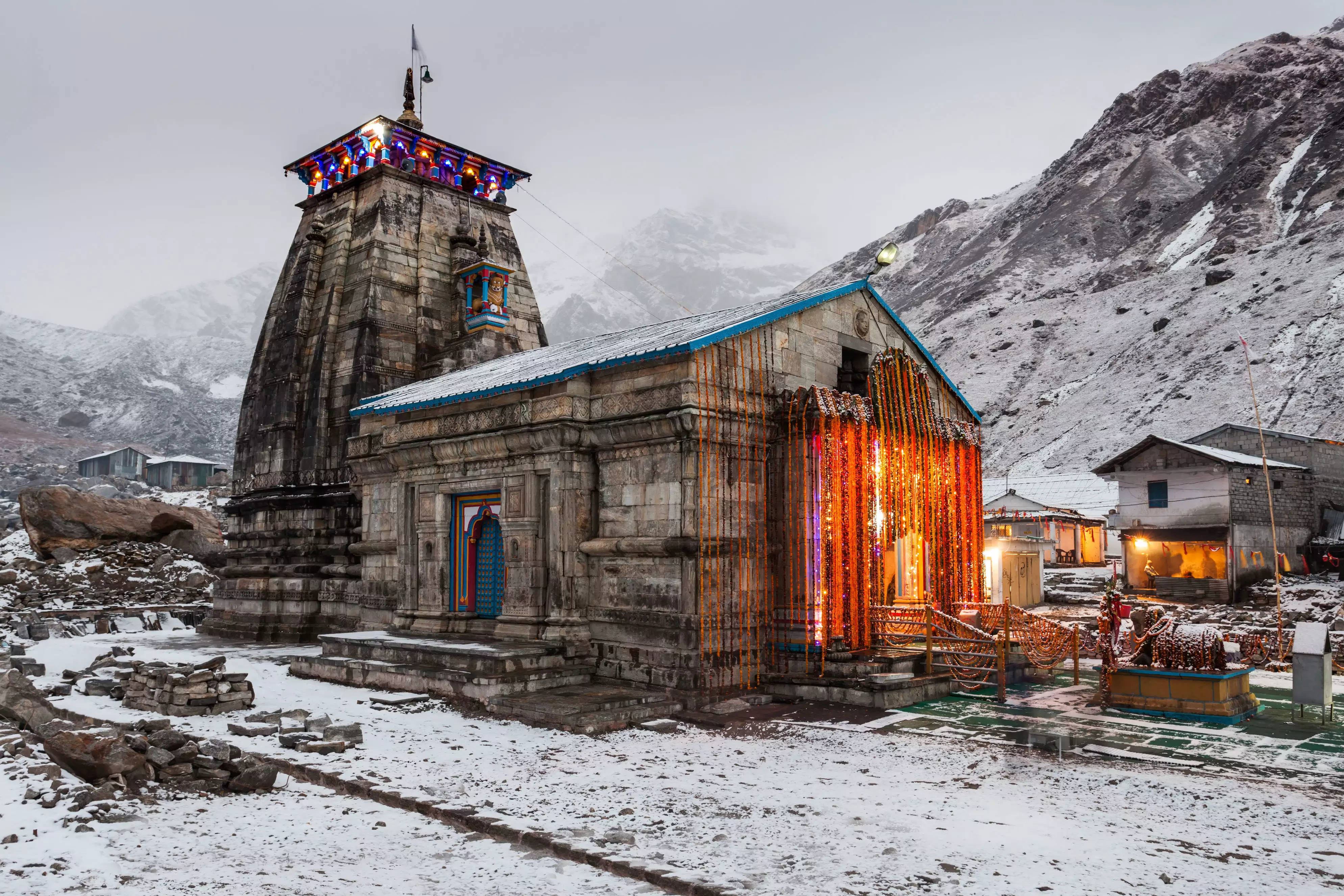 Kedarnath 桌布 壁紙 — 一座被雪覆蓋的石廟在燈串下溫暖地發光，背景是崎嶇的雪山。