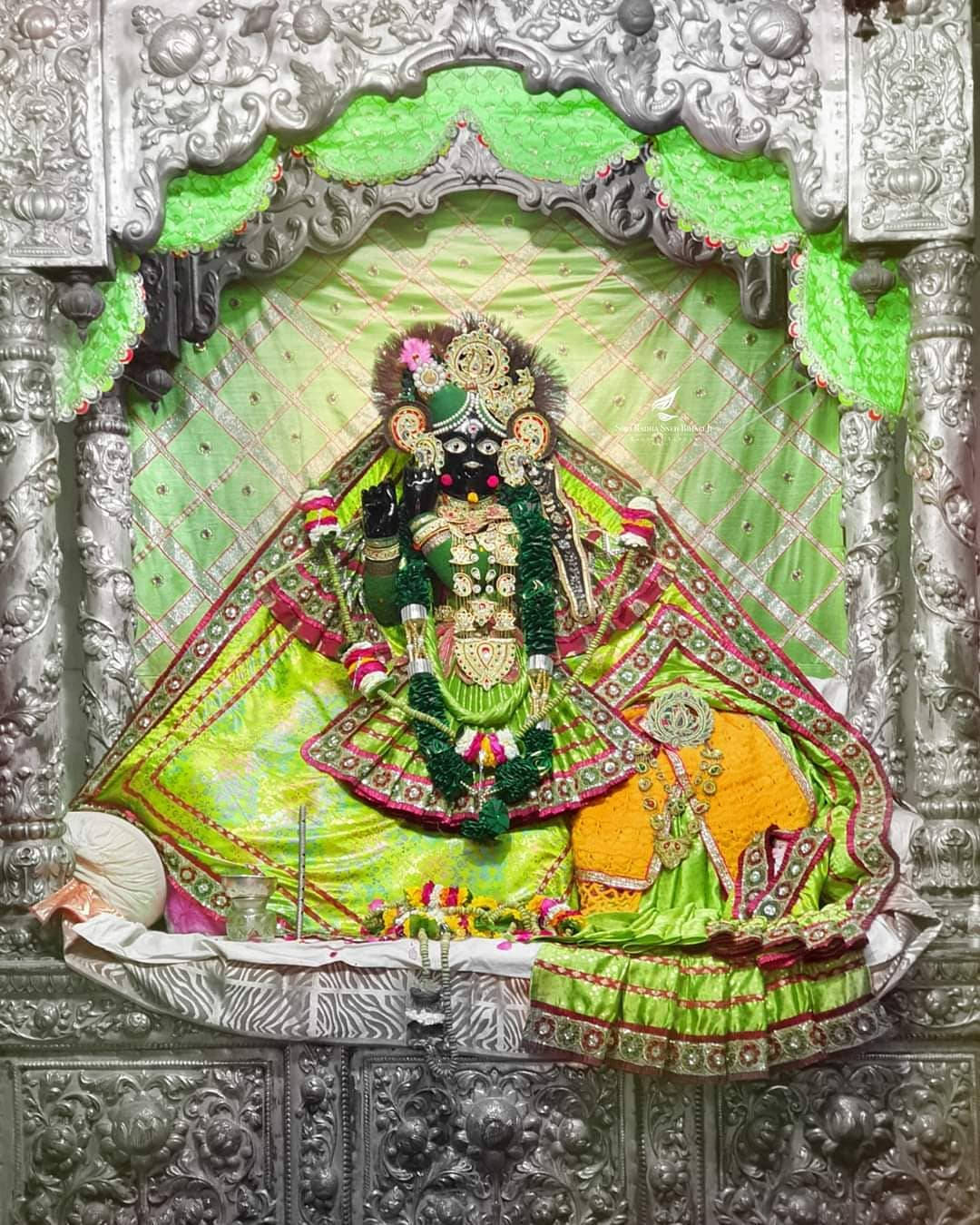 krishna god 桌布 壁紙 — 一座裝飾華麗的黑色神像端坐在一個飾有精緻銀色神龕內，神龕披掛著鮮綠色布料。