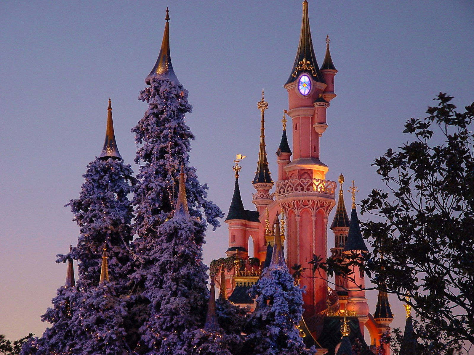 Disneyland 桌布 壁紙 — 一座覆蓋著白雪的城堡，閃爍的塔樓聳立在暮色天空下，四周環繞著結霜的樹木。