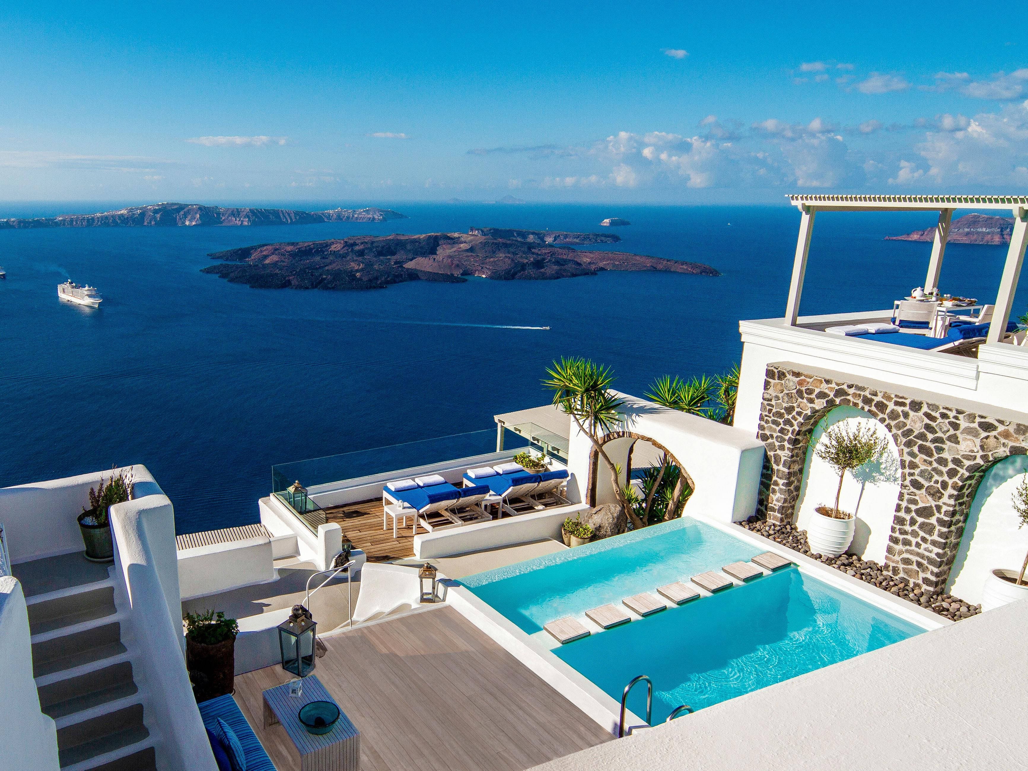 Santorini 桌布 壁紙 — 一座豪華白色別墅，擁有碧綠色的游泳池，俯瞰深藍色的愛琴海和火山島，在明亮的藍天下。