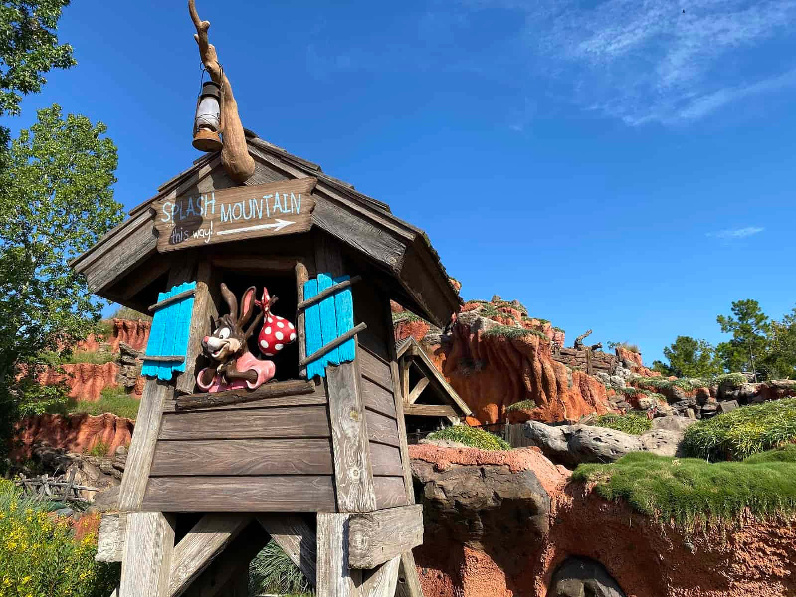 Splash Mountain 桌布 壁紙 — 一座質樸的木塔，上面有寫著「飛濺山此路」的標誌，有一隻卡通兔子和老鼠在紅色岩石懸崖和藍天背景下探出頭來。