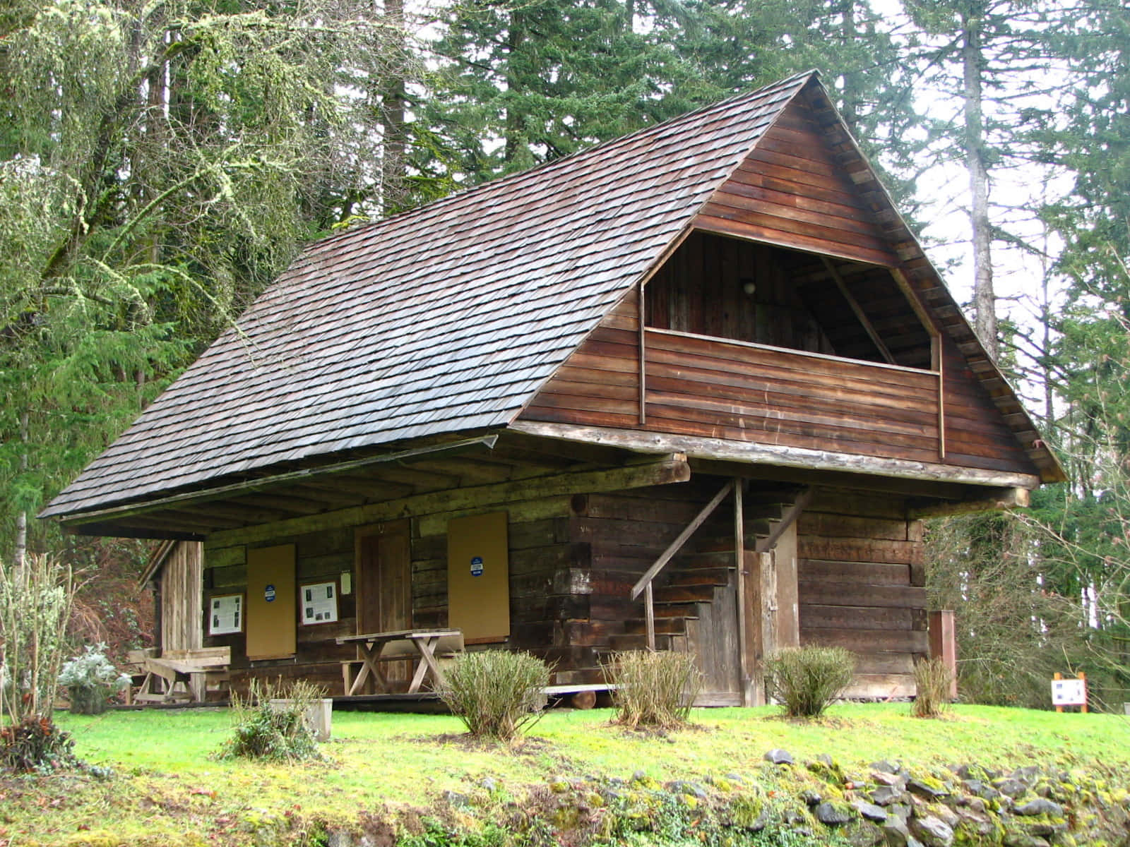 Log Cabin 桌布 壁紙 — 一座質樸的木屋，擁有陡峭的屋頂和開放的閣樓，坐落在寧靜森林空地上高大的苔蘚樹木之間。