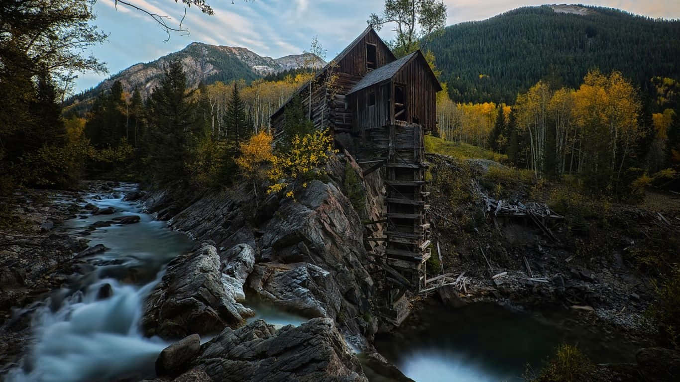 Colorado Mountains 桌布 壁紙 — 一座質樸的木製水車磨坊坐落在秋日山間急流旁的岩石懸崖上。