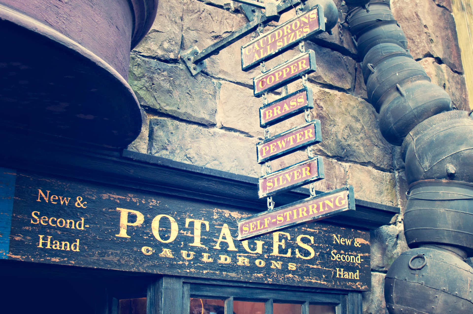 Hogsmeade 桌布 壁紙 — 一座質樸的石頭建築展示了一個風化的招牌，上面寫著「Potages Cauldrons」，並掛有金屬招牌，列出銅、黃銅、錫和銀等材料。