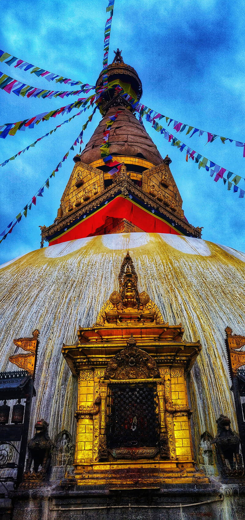 桌布 壁紙 — 一座金色佛塔，雕刻精緻，彩色經幡飄揚，映襯著戲劇性的藍天。