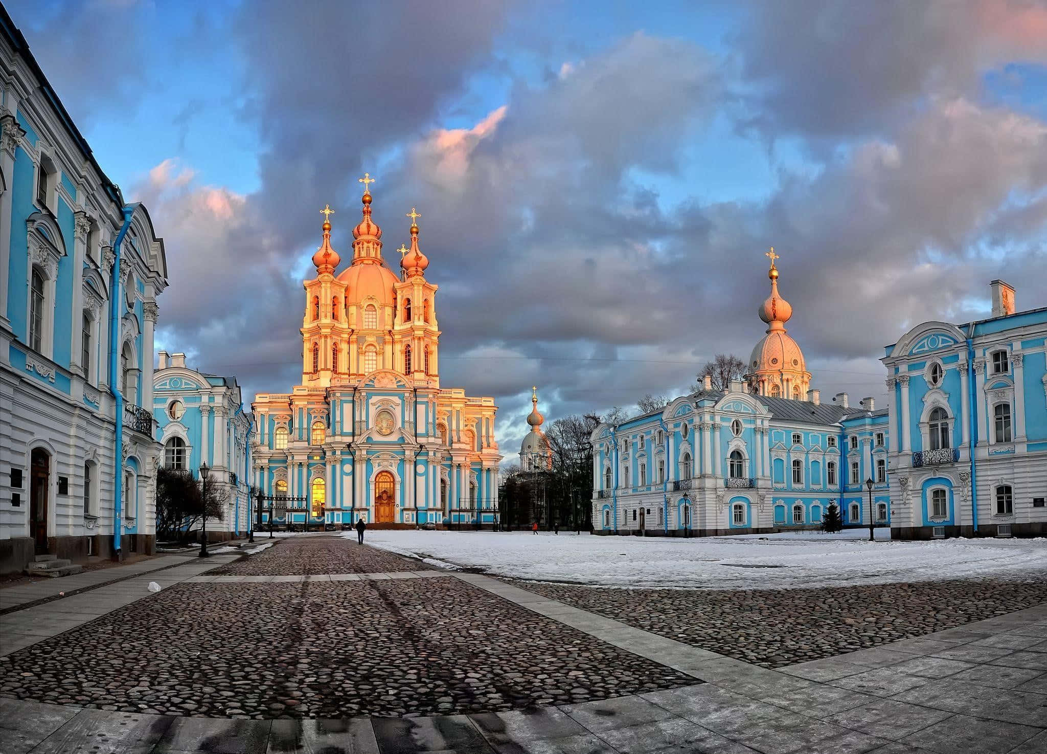 Russia 桌布 壁紙 — 一座金色圓頂大教堂和藍色巴洛克建築在暮色天空下溫暖地發光，積雪覆蓋著鵝卵石廣場。
