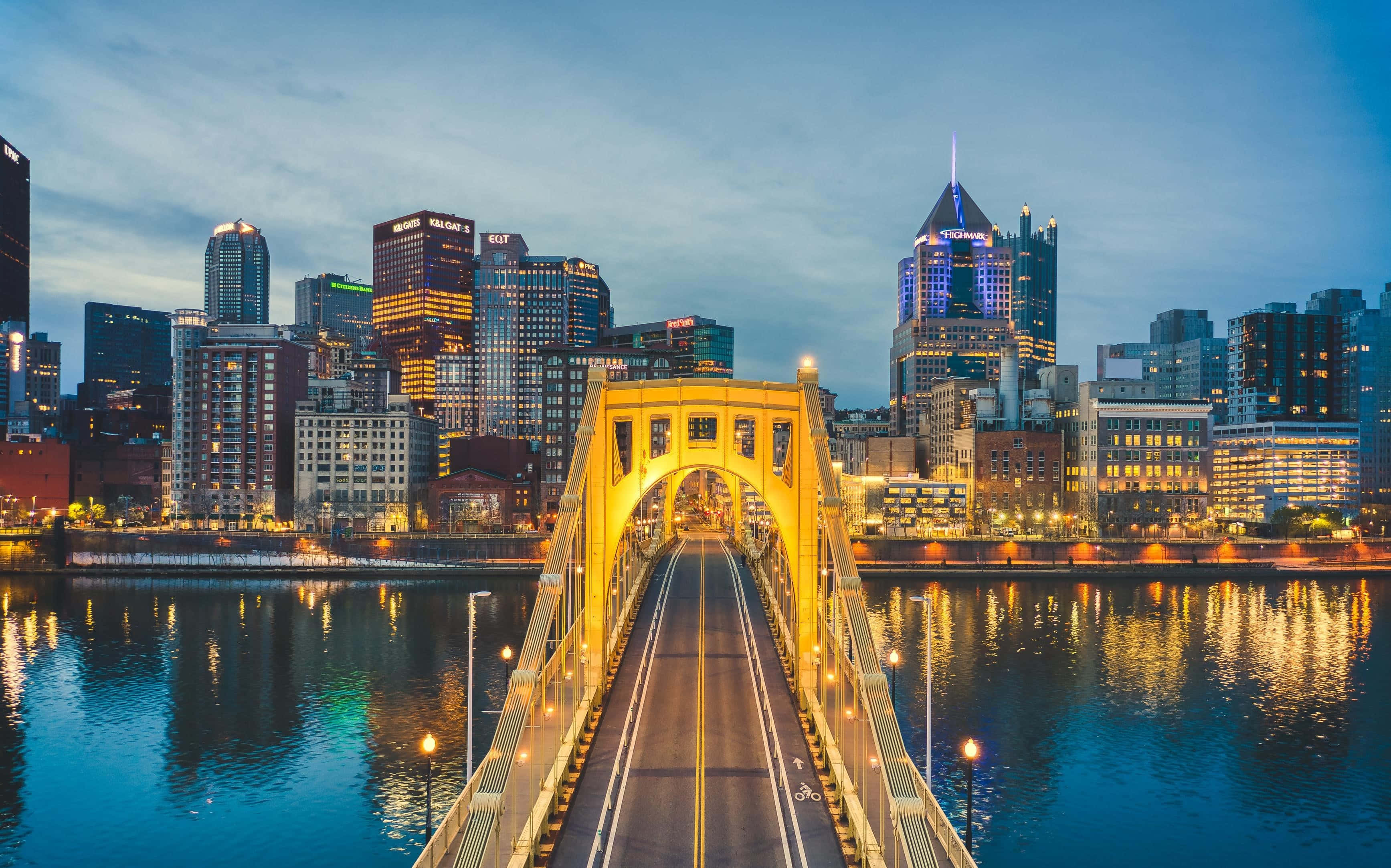 Pittsburgh Skyline 桌布 壁紙 — 一座金色的橋樑橫跨平靜的河流，通往暮色中閃耀的城市天際線。