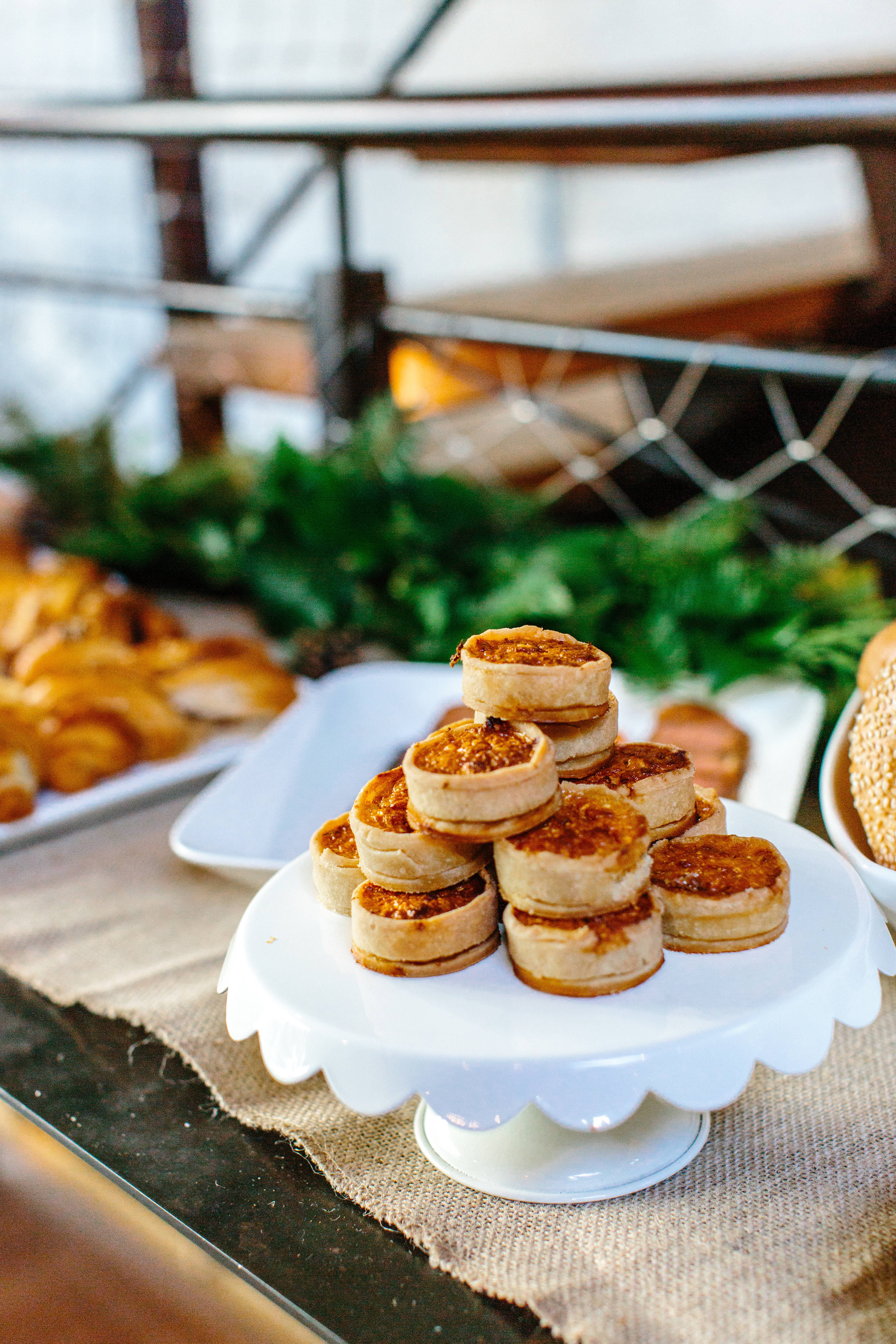Pastries 桌布 壁紙 — 一座金黃色迷你塔金字塔，頂部焦糖化，優雅地放在白色蛋糕架上，置於麻布桌布上。
