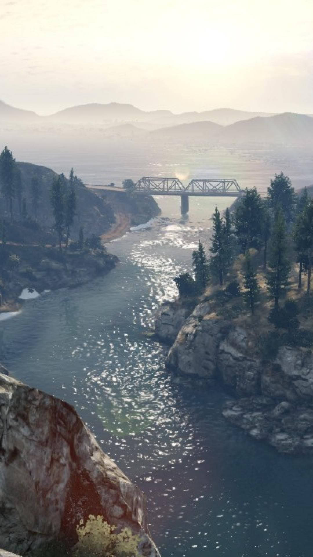 Grand Theft Auto V 桌布 壁紙 — 一座鋼製桁架橋橫跨蜿蜒的河流，穿過霧氣瀰漫的山脈，松樹和岩石峭壁沐浴在柔和的晨光中。