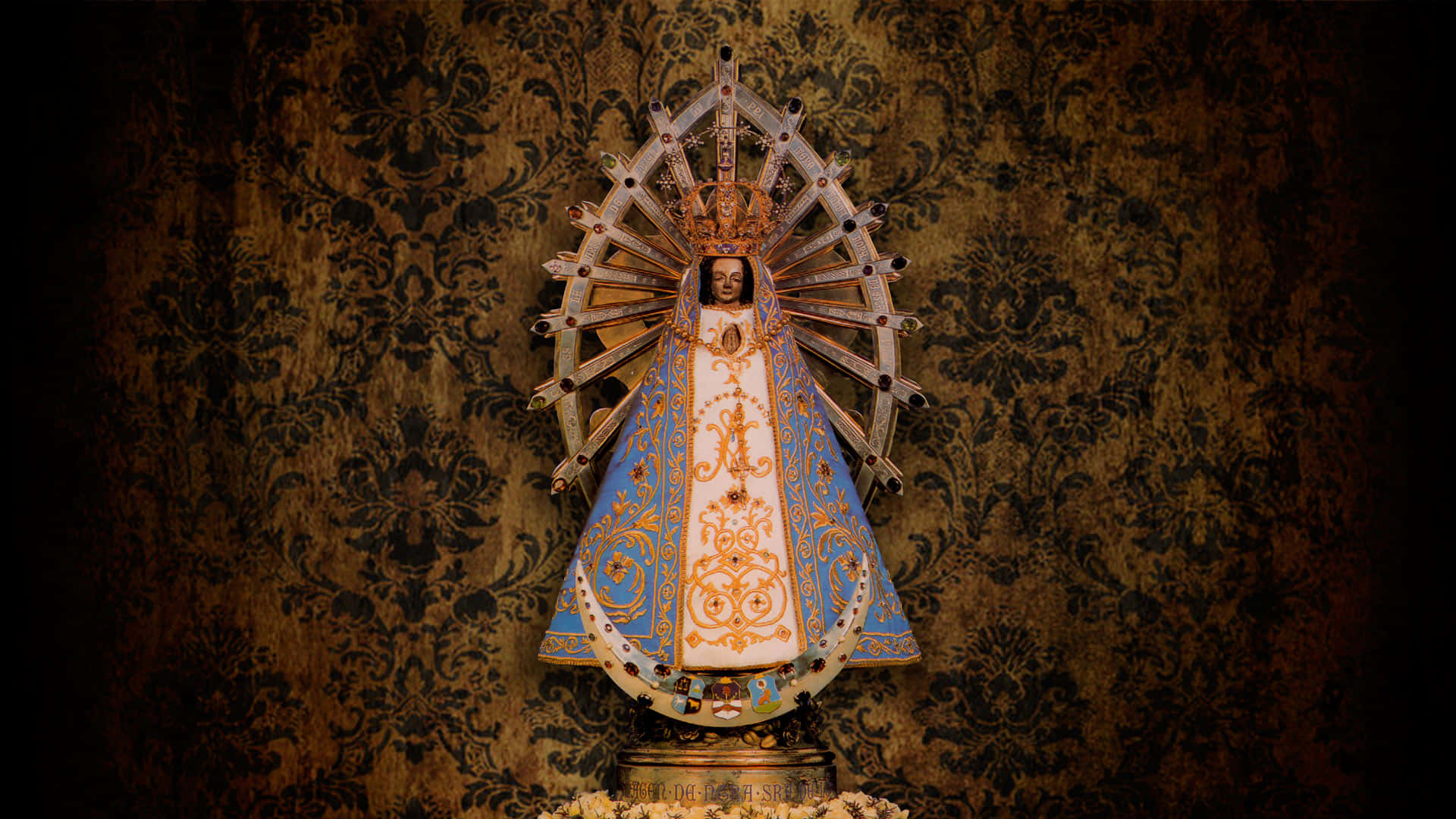 Catholic Desktop 桌布 壁紙 — 一座閃耀的聖母瑪利亞宗教雕像，戴著金色皇冠，身著華麗的藍白長袍，立於深色錦緞壁紙前。