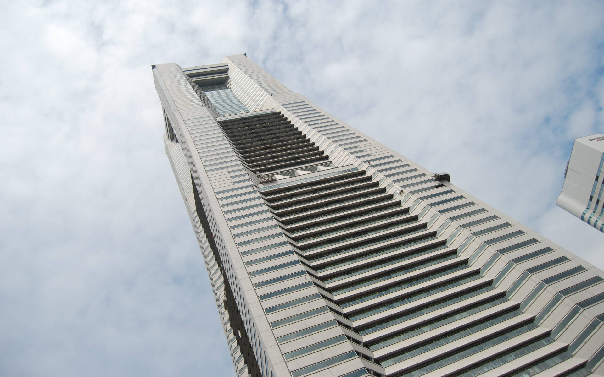 Yokohama 桌布 壁紙 — 一座階梯式玻璃幕牆的現代高聳摩天大樓在陰天中銳利地聳立。