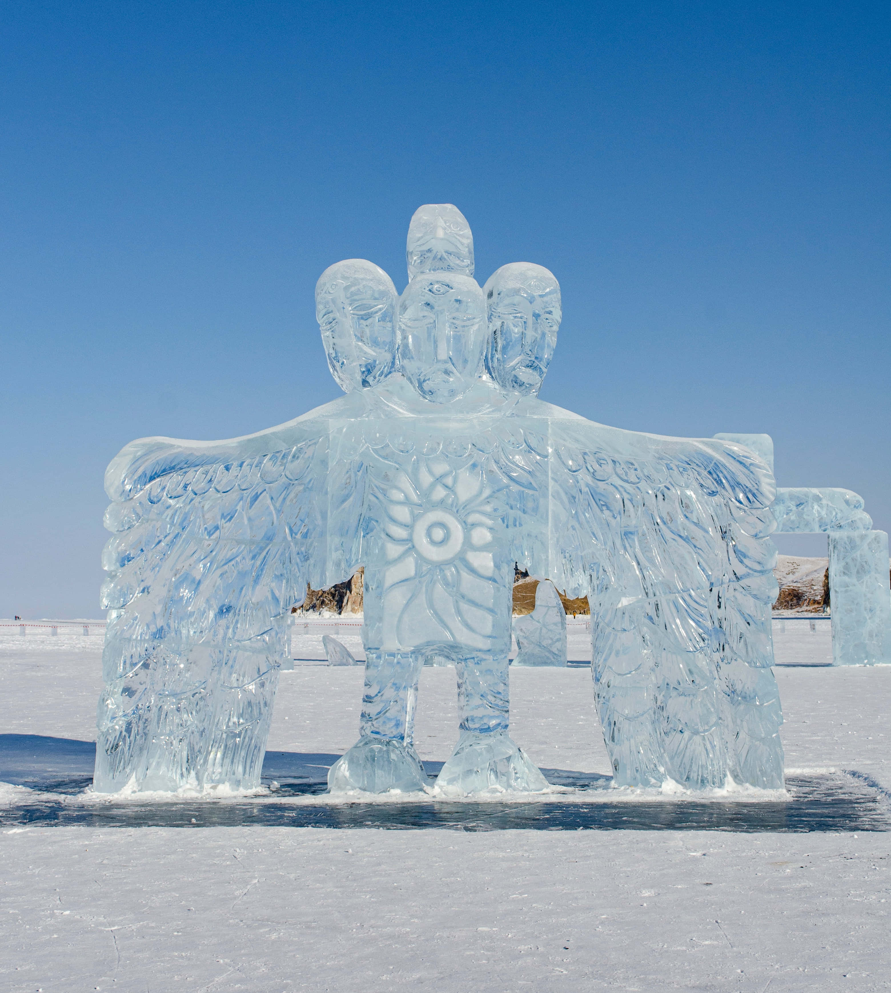 Ice Sculpture 桌布 壁紙 — 一座雄偉的三頭冰雕，展開翅膀，在冰凍平原上高聳於清澈的藍天之下。