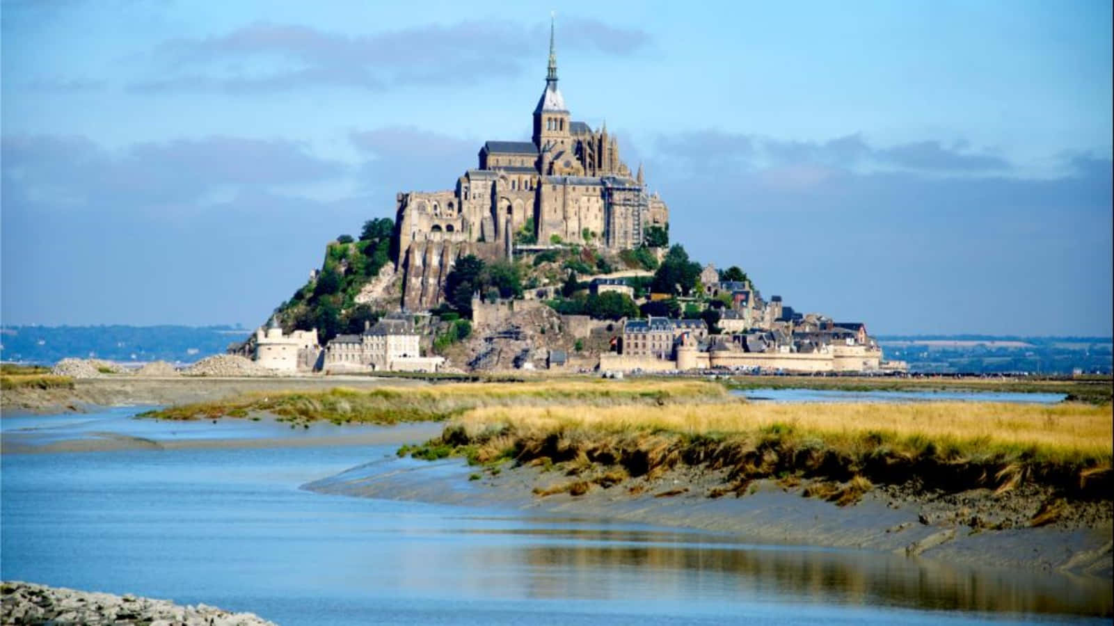 France 桌布 壁紙 — 一座雄偉的中世紀修道院坐落在岩石島上，周圍是潮汐灘塗，天空部分多雲。