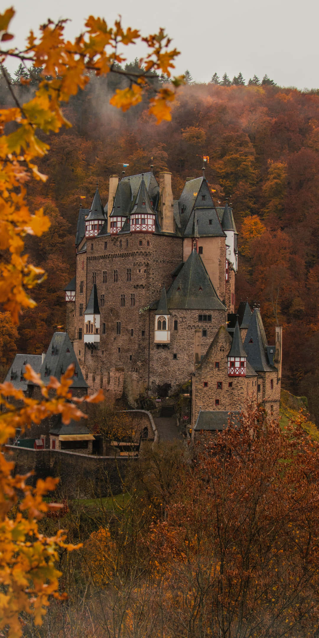 Pixel 3 Autumn 桌布 壁紙 — 一座雄偉的中世紀城堡坐落在山丘上，周圍環繞著鮮豔的秋葉，天空柔和多雲。