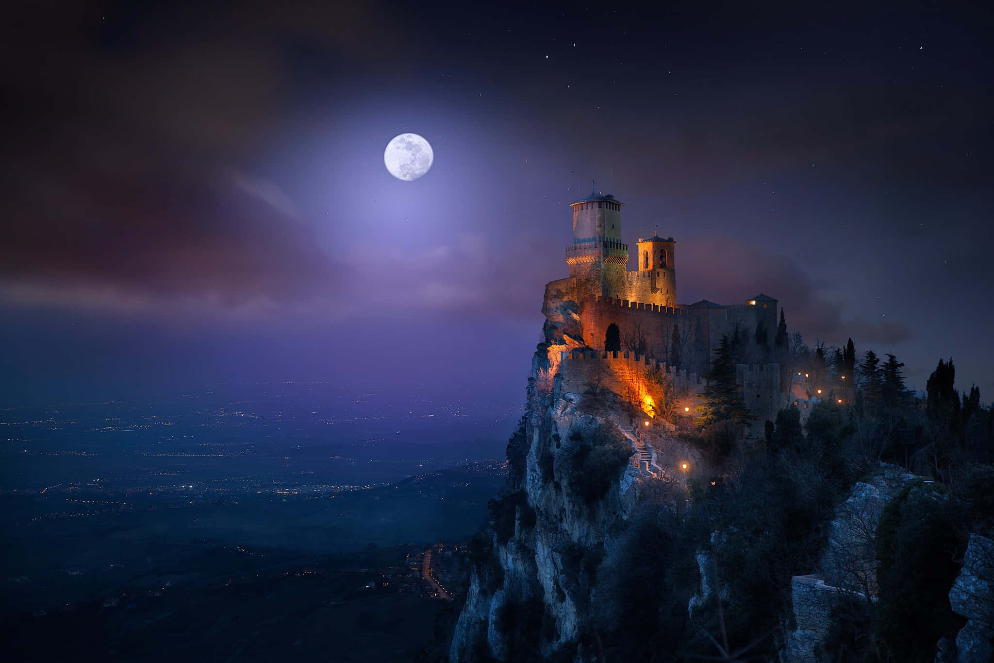 full moon 桌布 壁紙 — 一座雄偉的中世紀城堡坐落在懸崖上，在明亮的滿月下，為下方的山谷投下神秘的光芒。