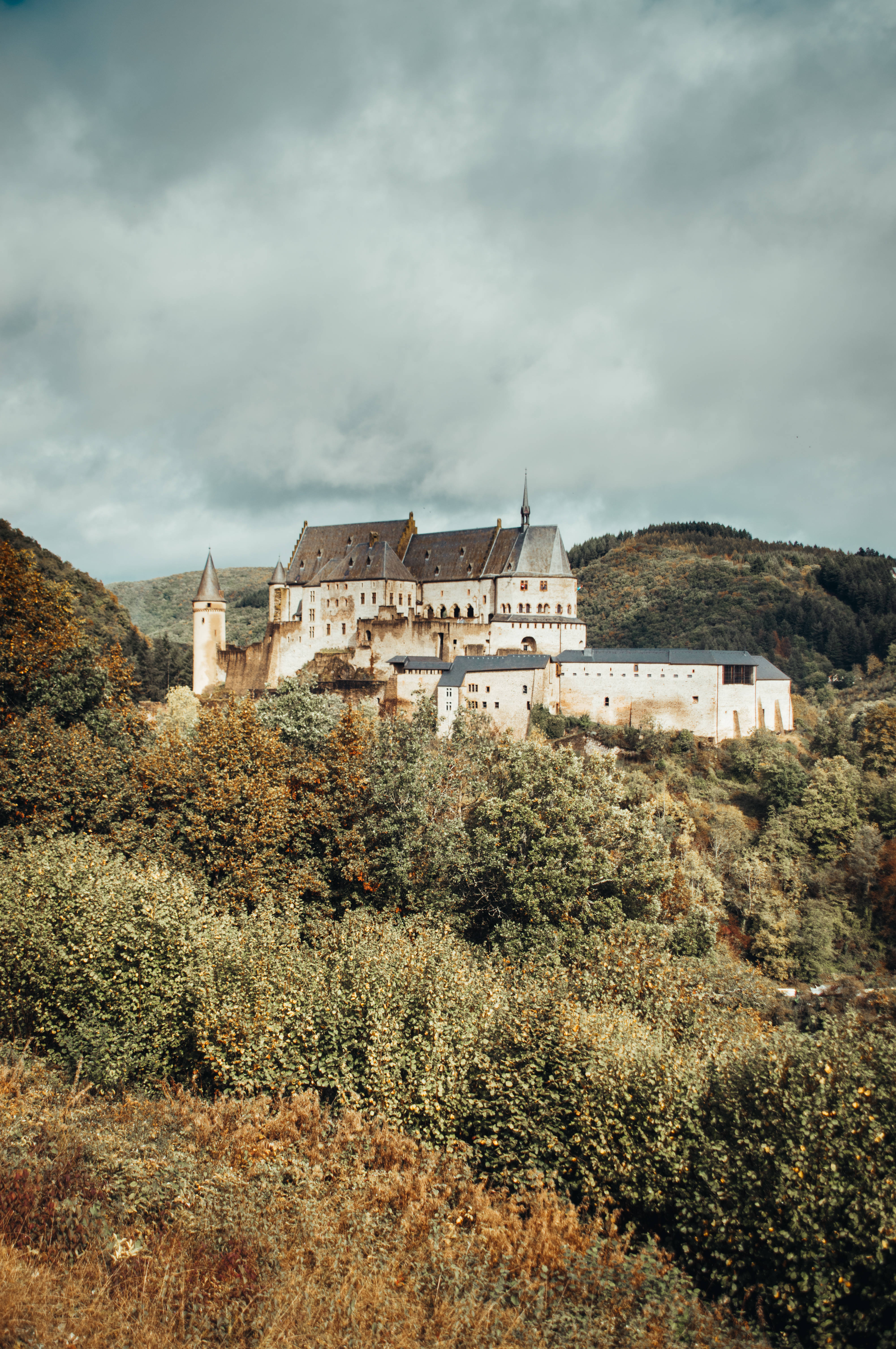 Luxembourg 桌布 壁紙 — 一座雄偉的中世紀城堡坐落在森林覆蓋的山丘上，天空陰沉多雲。