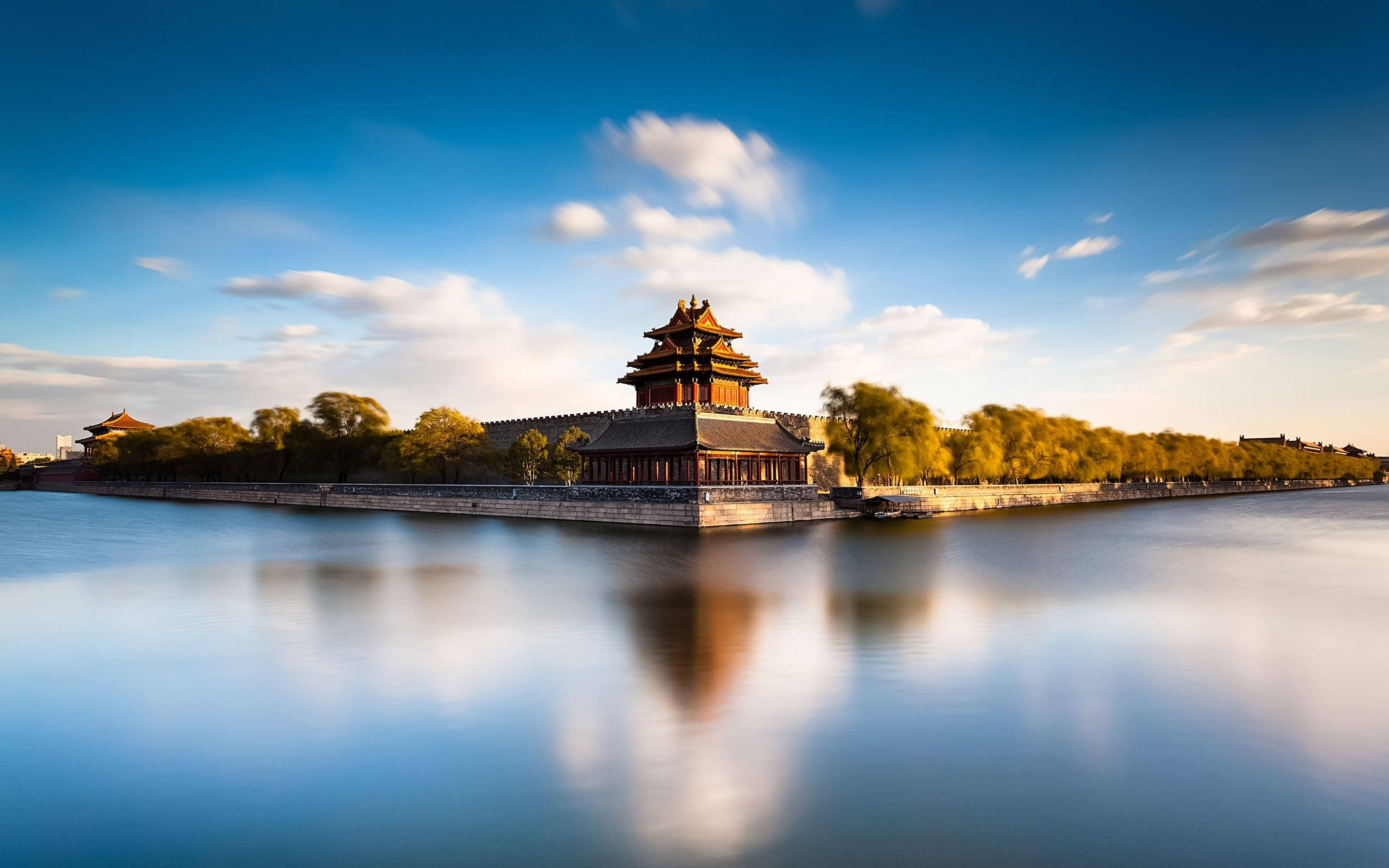 Beijing 桌布 壁紙 — 一座雄偉的傳統中國宮殿塔樓在平靜的水面上寧靜地倒映，天空湛藍，雲朵柔和。