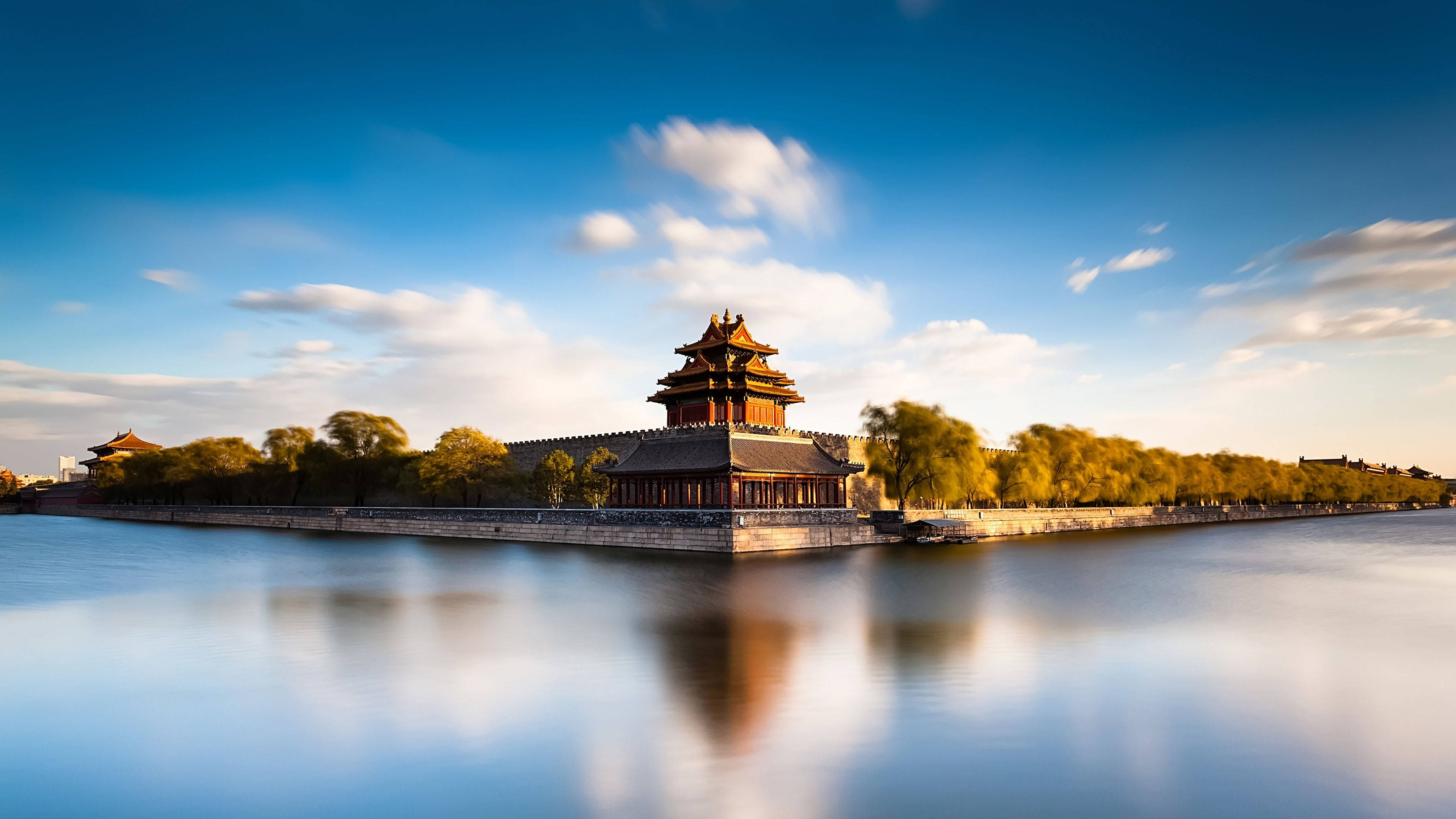 Travel And Tourism 桌布 壁紙 — 一座雄偉的傳統中國宮殿塔樓靜靜地矗立在平靜的護城河上，上方是帶有柔和雲朵的湛藍天空。