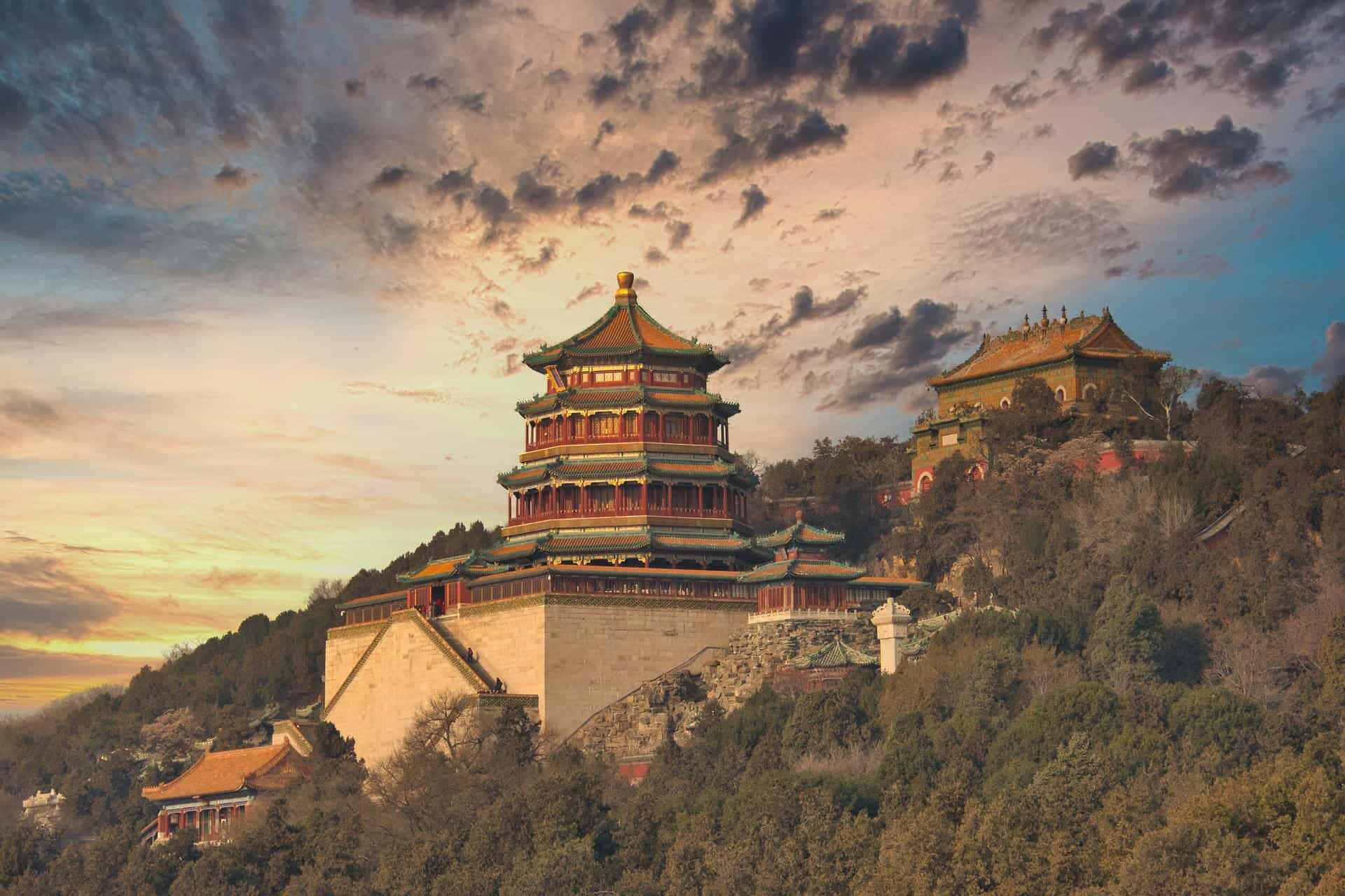 Cloud Aesthetic 桌布 壁紙 — 一座雄偉的傳統中式寶塔，坐落在森林覆蓋的山丘上，背景是壯麗的日落天空。