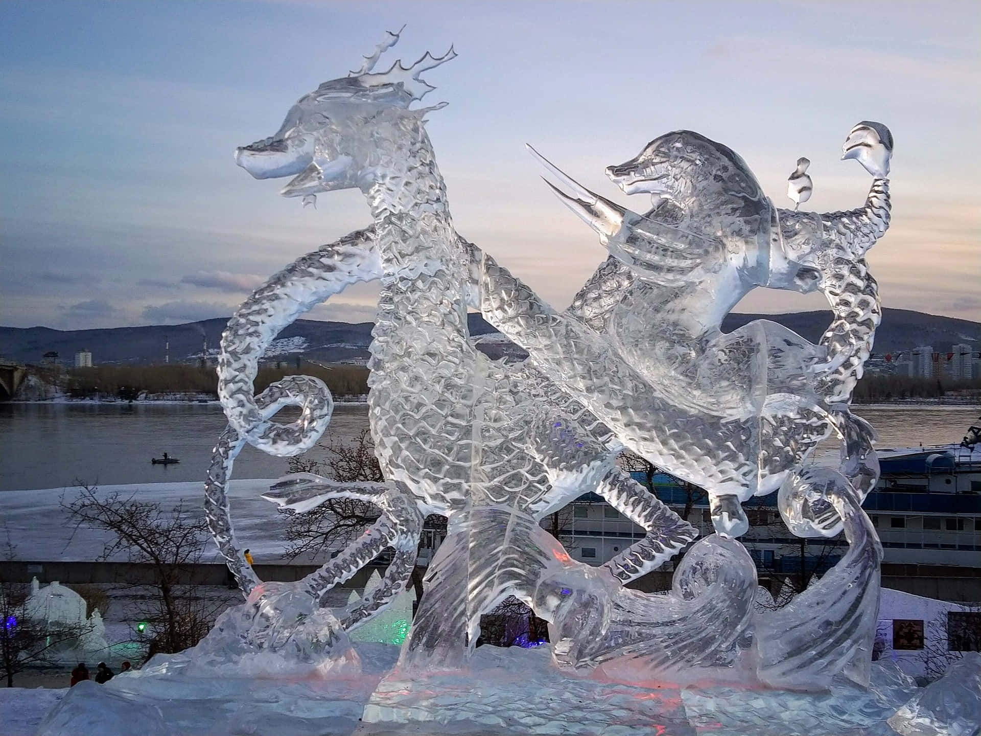 Ice Sculpture 桌布 壁紙 — 一座雄偉的冰龍雕塑在暮色天空下，靠近冰封的河流，內部燈光閃爍發光。