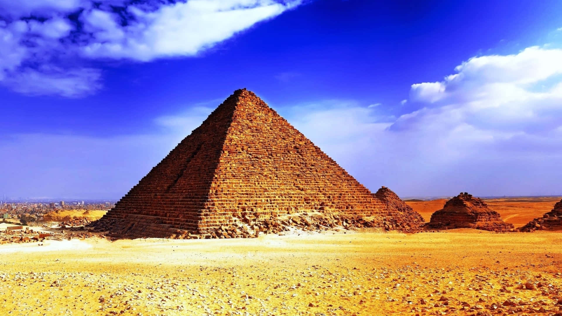 Ancient Egypt 桌布 壁紙 — 一座雄偉的古金字塔從金色沙漠中升起，在蔚藍的天空下，點綴著幾朵雲彩。
