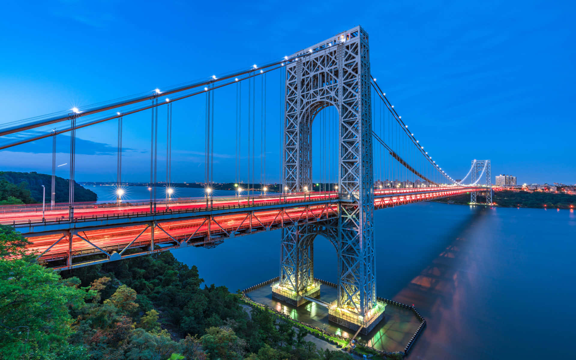 New York City 4K Ultra HD 桌布 壁紙 — 一座雄偉的吊橋在深藍色天空下的黃昏時分，在水面上閃爍著紅色的光跡。