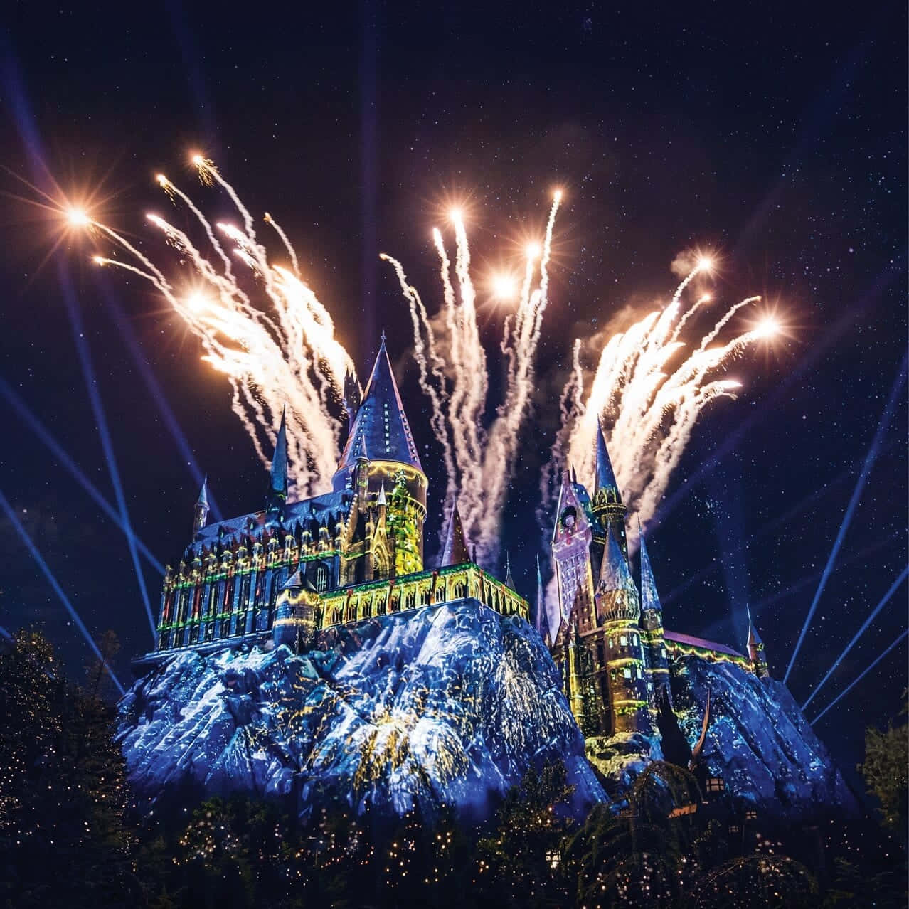 Christmas At Hogwarts 桌布 壁紙 — 一座雄偉的城堡，在繁星點點的夜空下，被鮮豔的燈光和爆炸的煙火照亮。