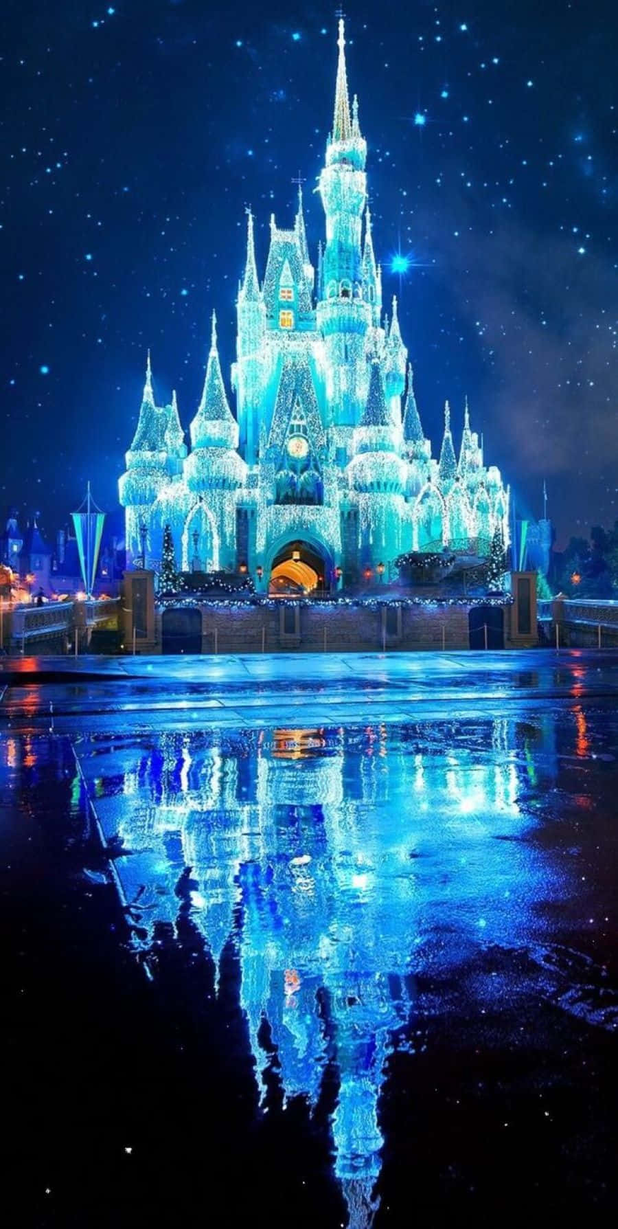 Aesthetic Disney 桌布 壁紙 — 一座雄偉的城堡在星空下閃耀著冰藍色的光芒，其倒影在下方濕漉漉的路面上閃爍。