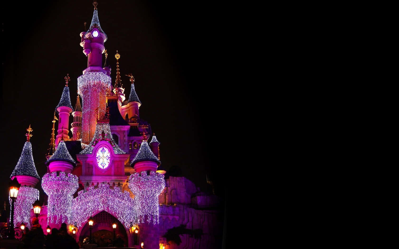 Disney World Desktop 桌布 壁紙 — 一座雄偉的城堡在漆黑的夜空下，被鮮豔的紫色和白色燈光照亮。