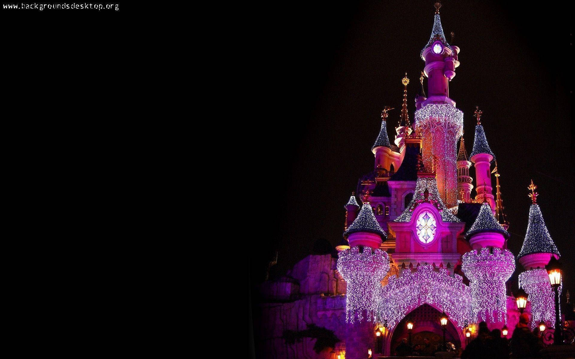 Disneyland Castle 桌布 壁紙 — 一座雄偉的城堡在漆黑的夜空下被鮮豔的紫色和白色燈光照亮。