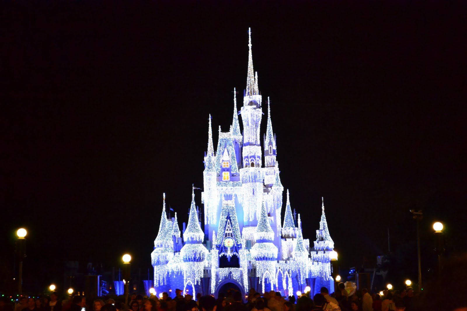 Disneyland Castle 桌布 壁紙 — 一座雄偉的城堡在黑暗的夜空中被鮮豔的藍色燈光照亮，下方聚集著人群。