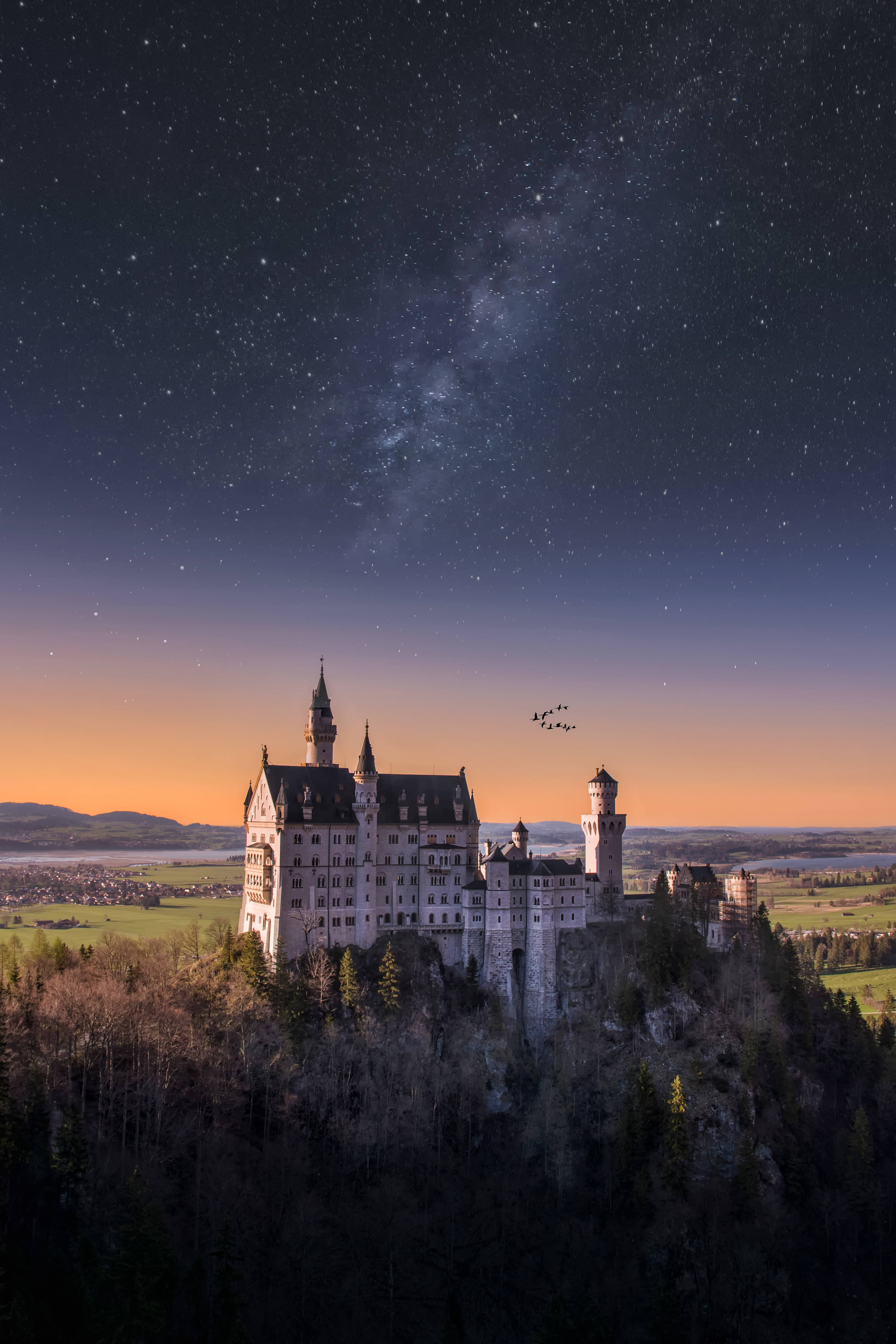Neuschwanstein Castle 桌布 壁紙 — 一座雄偉的城堡坐落在懸崖上，星空下閃耀著橙色的地平線。