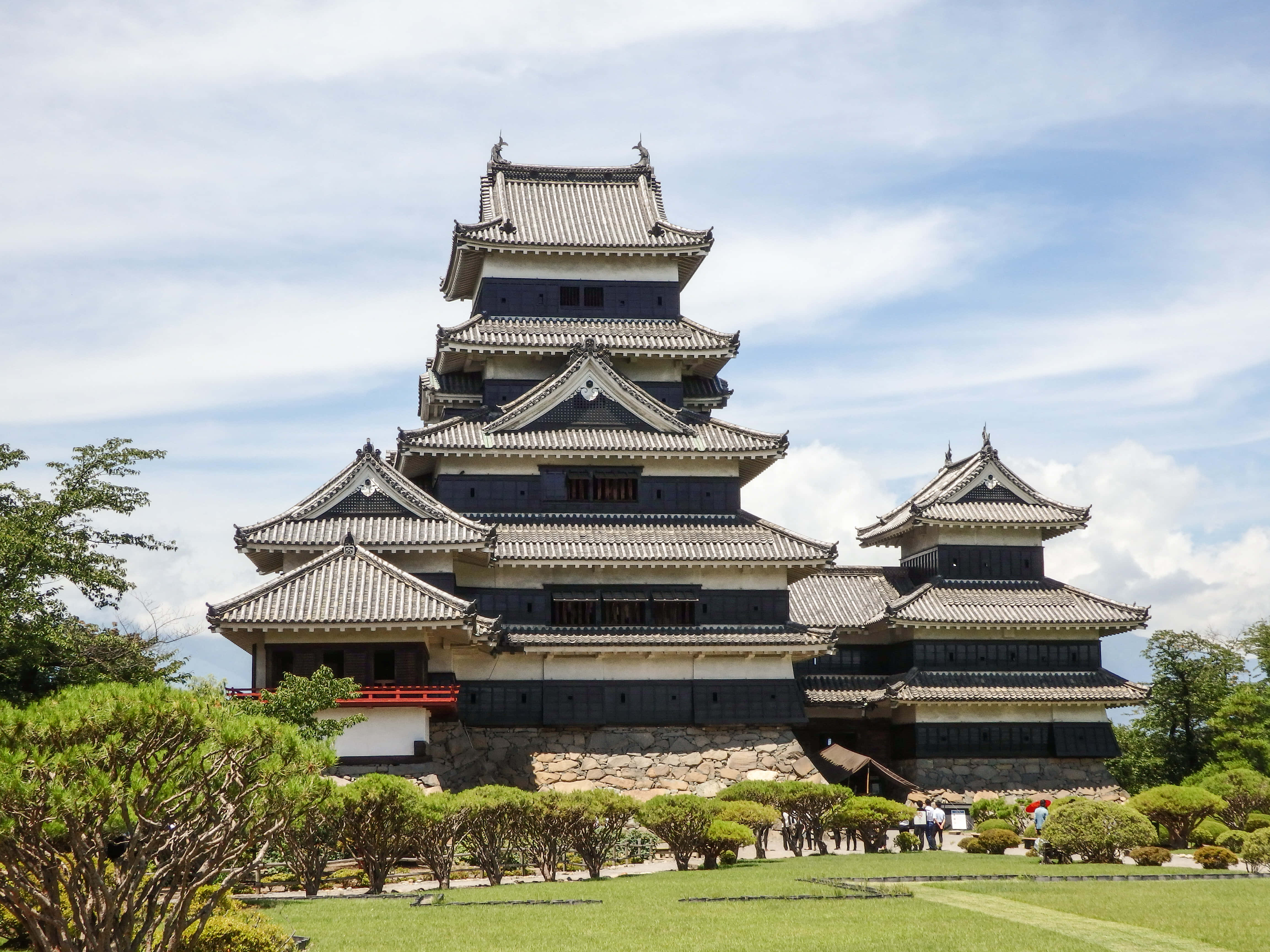 日本 桌布 壁紙 — 一座雄偉的多層日本城堡，擁有深色木牆和灰色瓦片屋頂，在藍天白雲下高高聳立。
